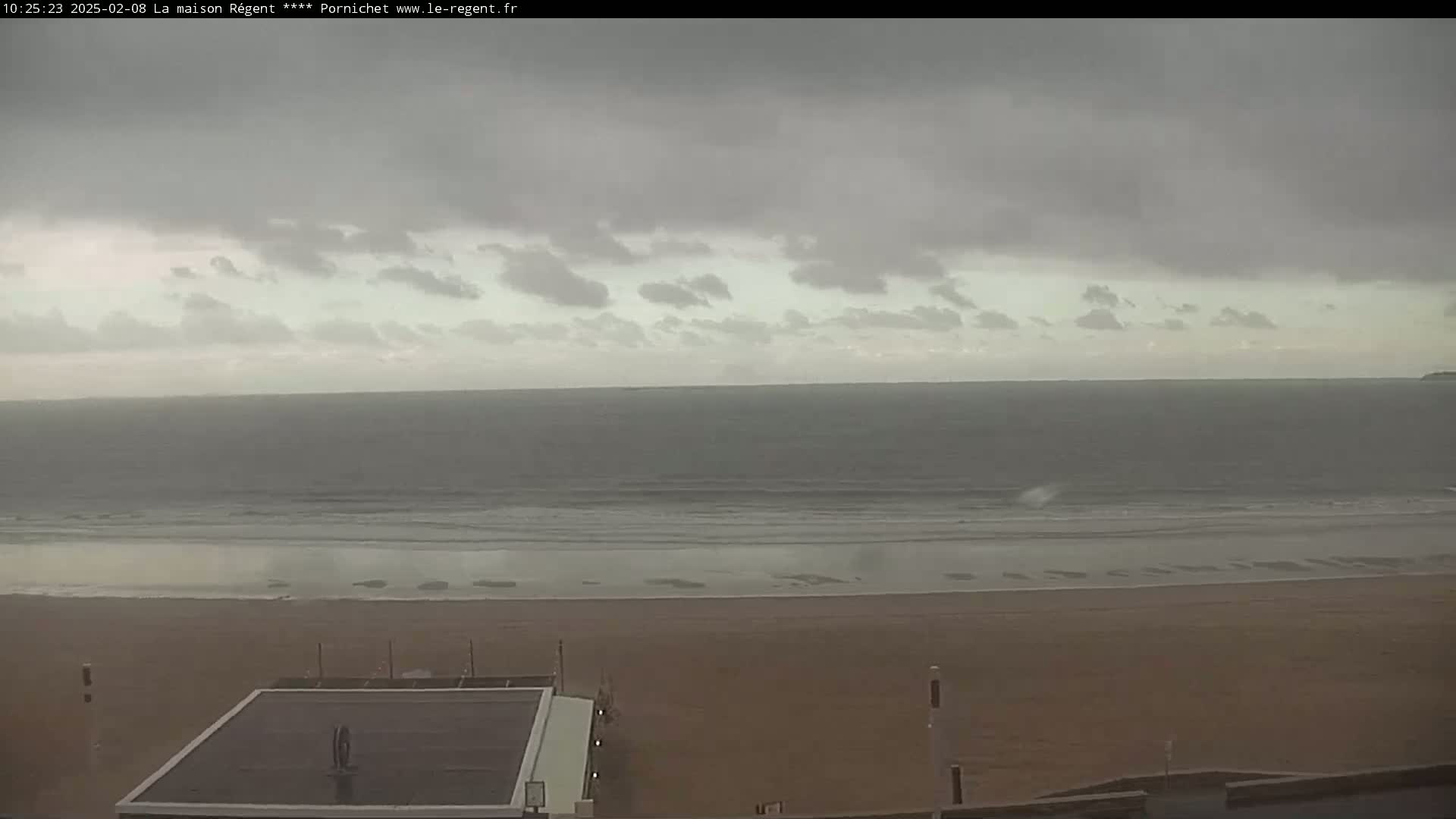 An overcast sky hangs over a wide, sandy beach and a calm, gray ocean.