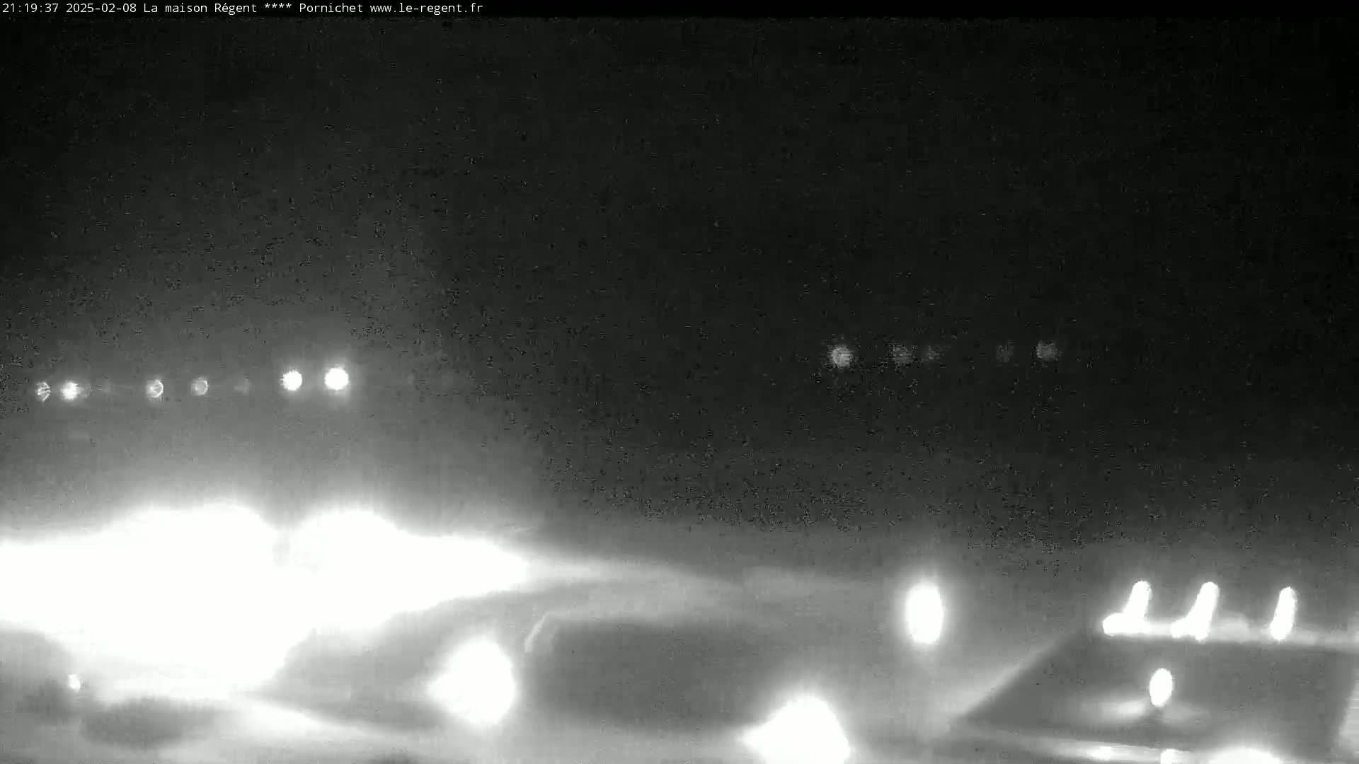 A nighttime, low-visibility scene shows several vehicles' headlights on a road, possibly in foggy or snowy conditions.