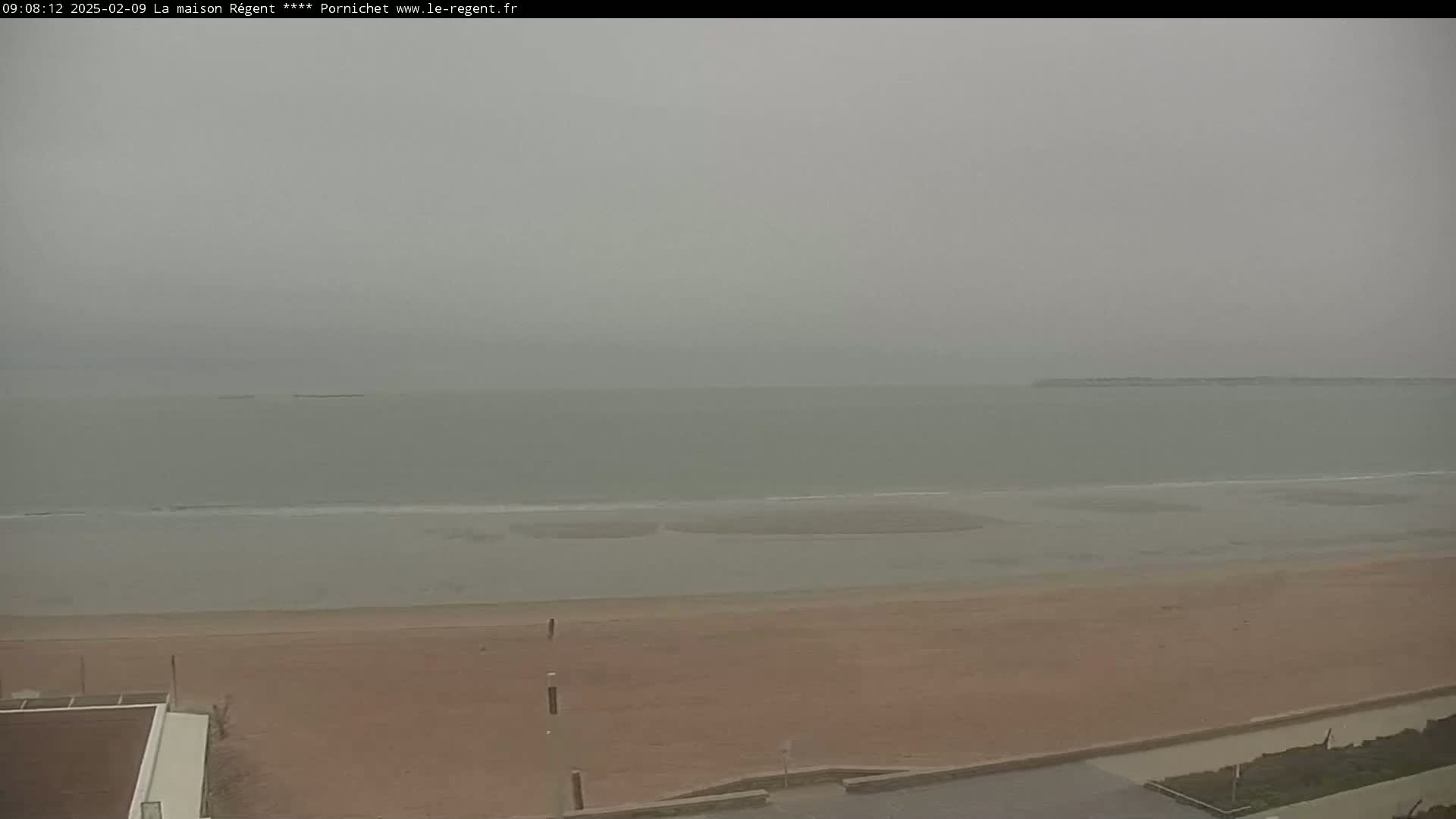 A hazy, overcast day reveals a wide, sandy beach meeting a calm, grey ocean.
