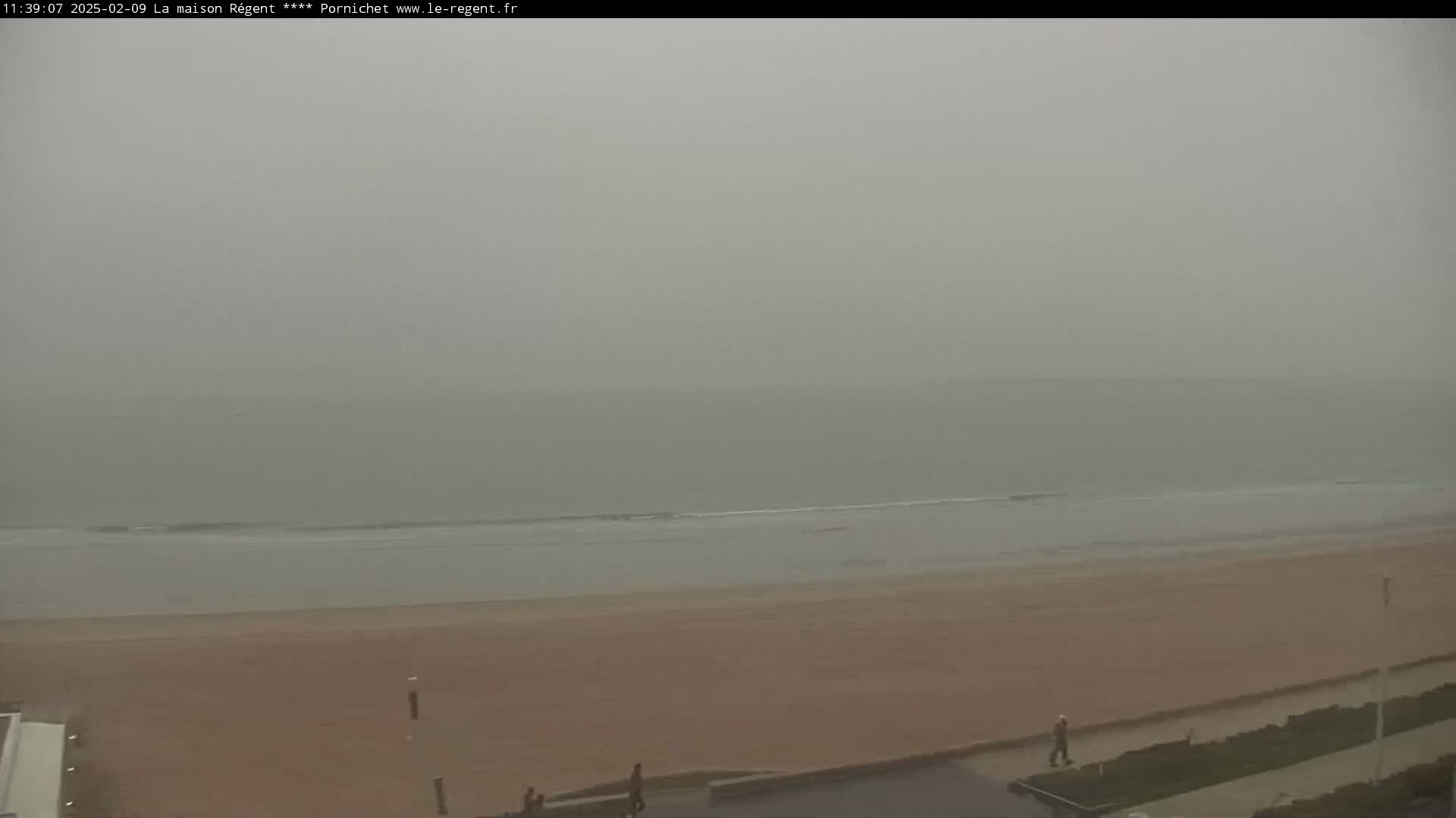 A hazy, overcast day reveals a wide sandy beach and calm ocean waves.