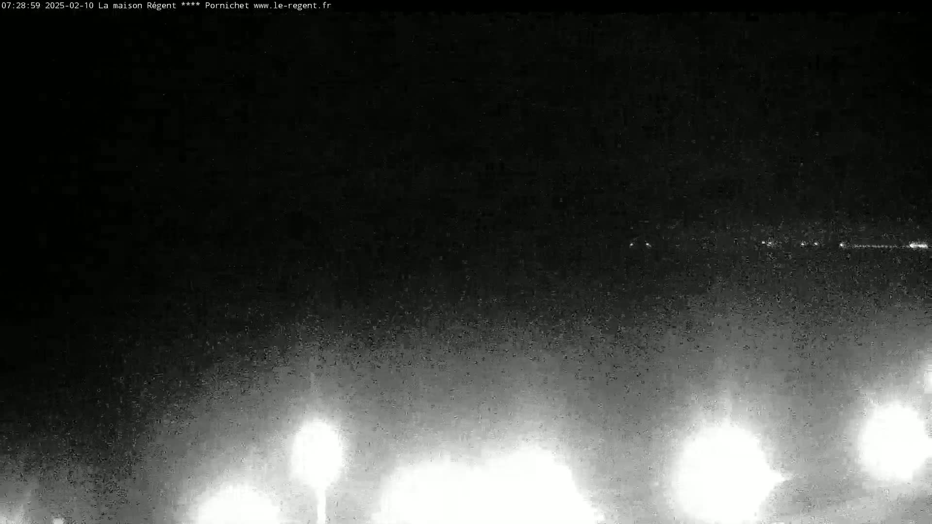 A nighttime, low-light image shows a dark sky with a faint horizon line illuminated by several distant lights and bright lights closer to the viewer's perspective.