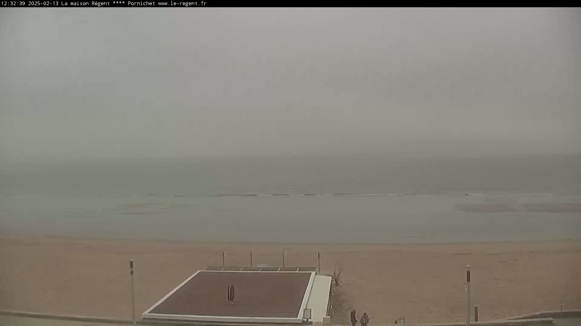A hazy view shows a beach with a flat, dark-colored structure on the sand and a calm, gray ocean in the background.