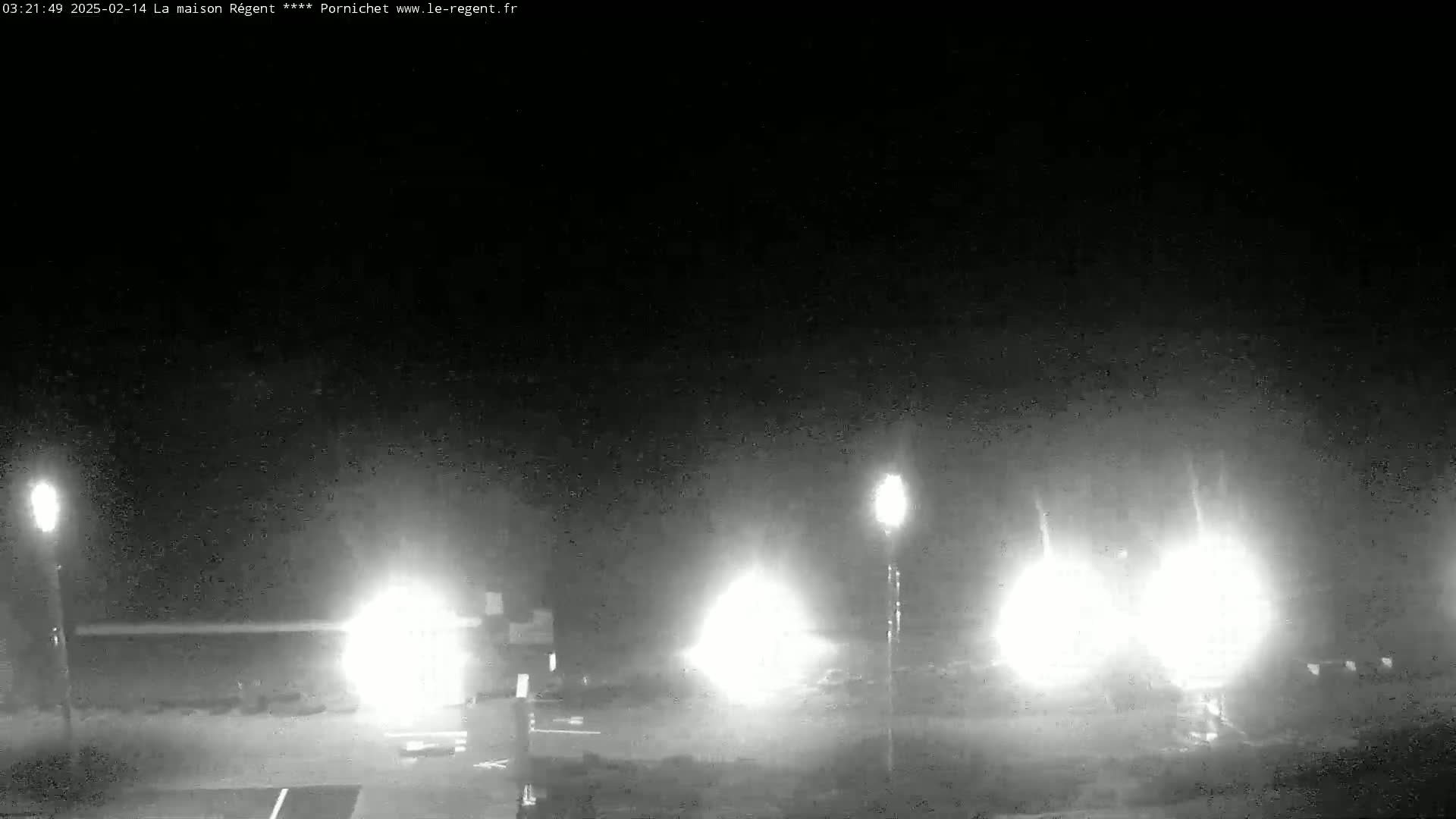 A nighttime, low-light view of a parking lot with several bright lights and some vehicles.