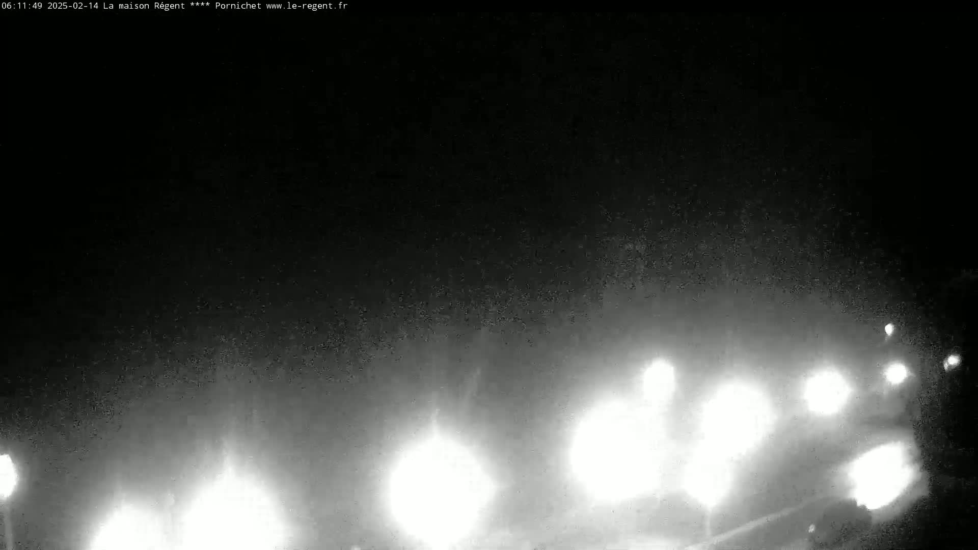 At night, under a dark, possibly foggy sky, the headlights of several vehicles are visible in the distance.