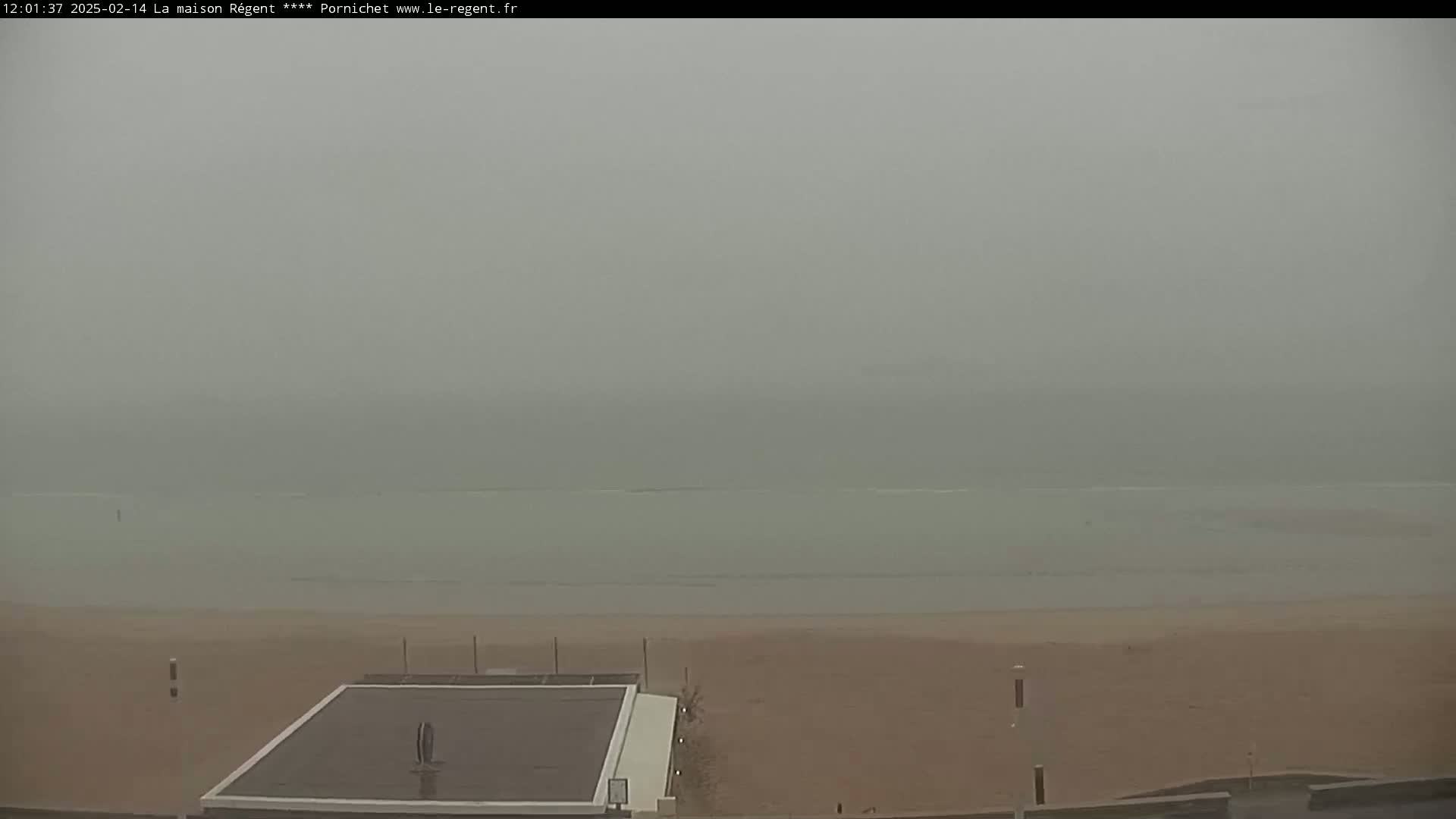 A hazy, overcast day shows a sandy beach and calm ocean water, viewed from a slightly elevated position.