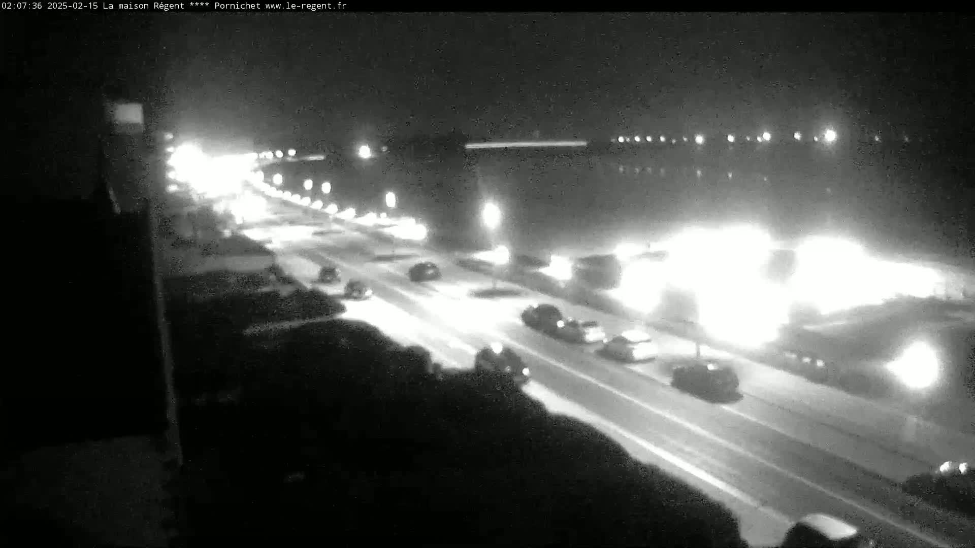 A nighttime, snowy scene shows a multi-lane road with cars driving in both directions, lit by streetlights and headlights.
