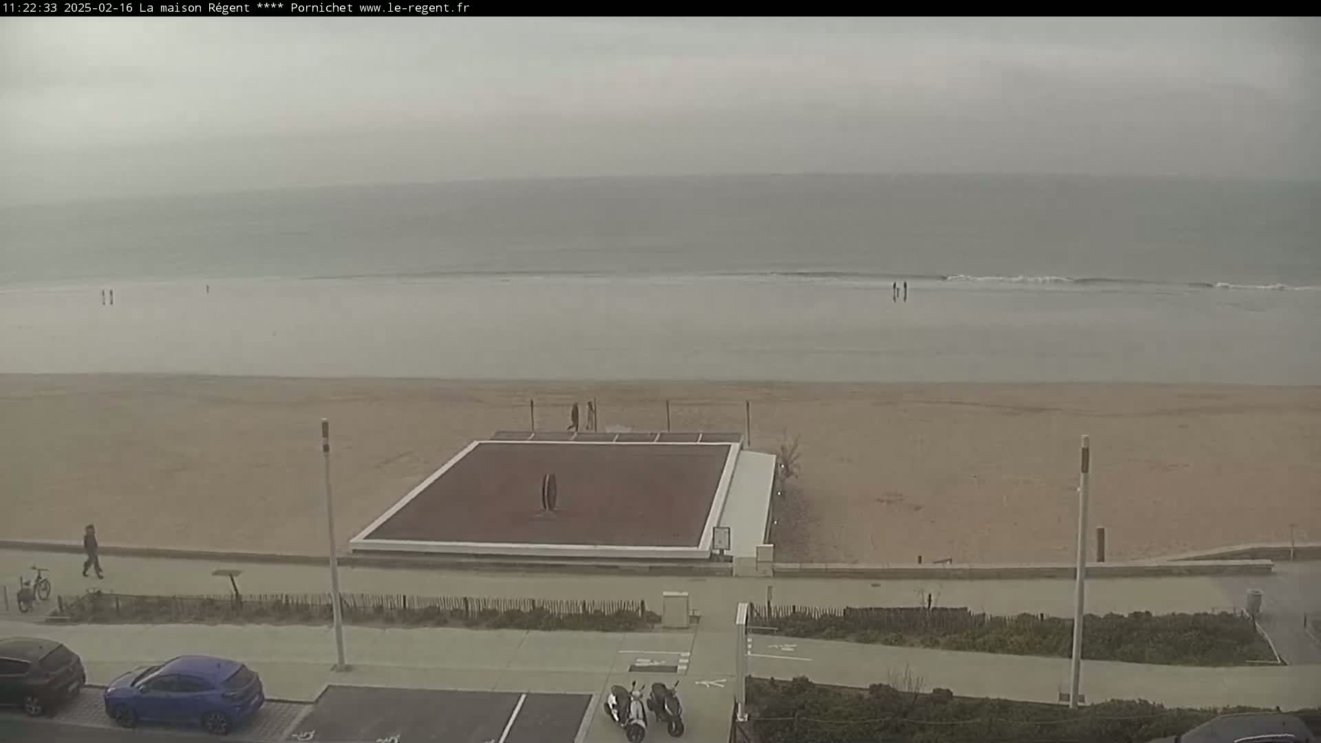 A mostly empty beach with a flat, dark-colored structure on the sand is visible under an overcast sky.