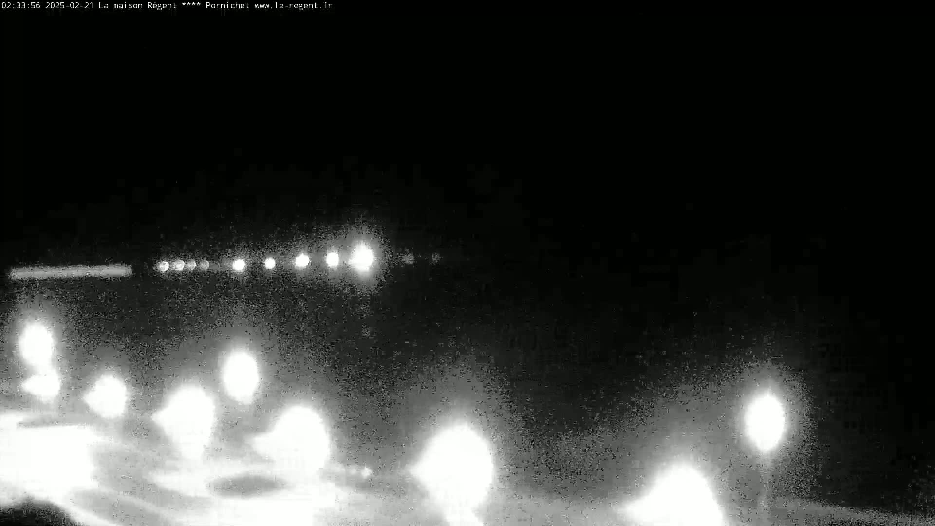 A nighttime, low-light image shows the headlights of numerous vehicles driving on a road, possibly in snowy or icy conditions.