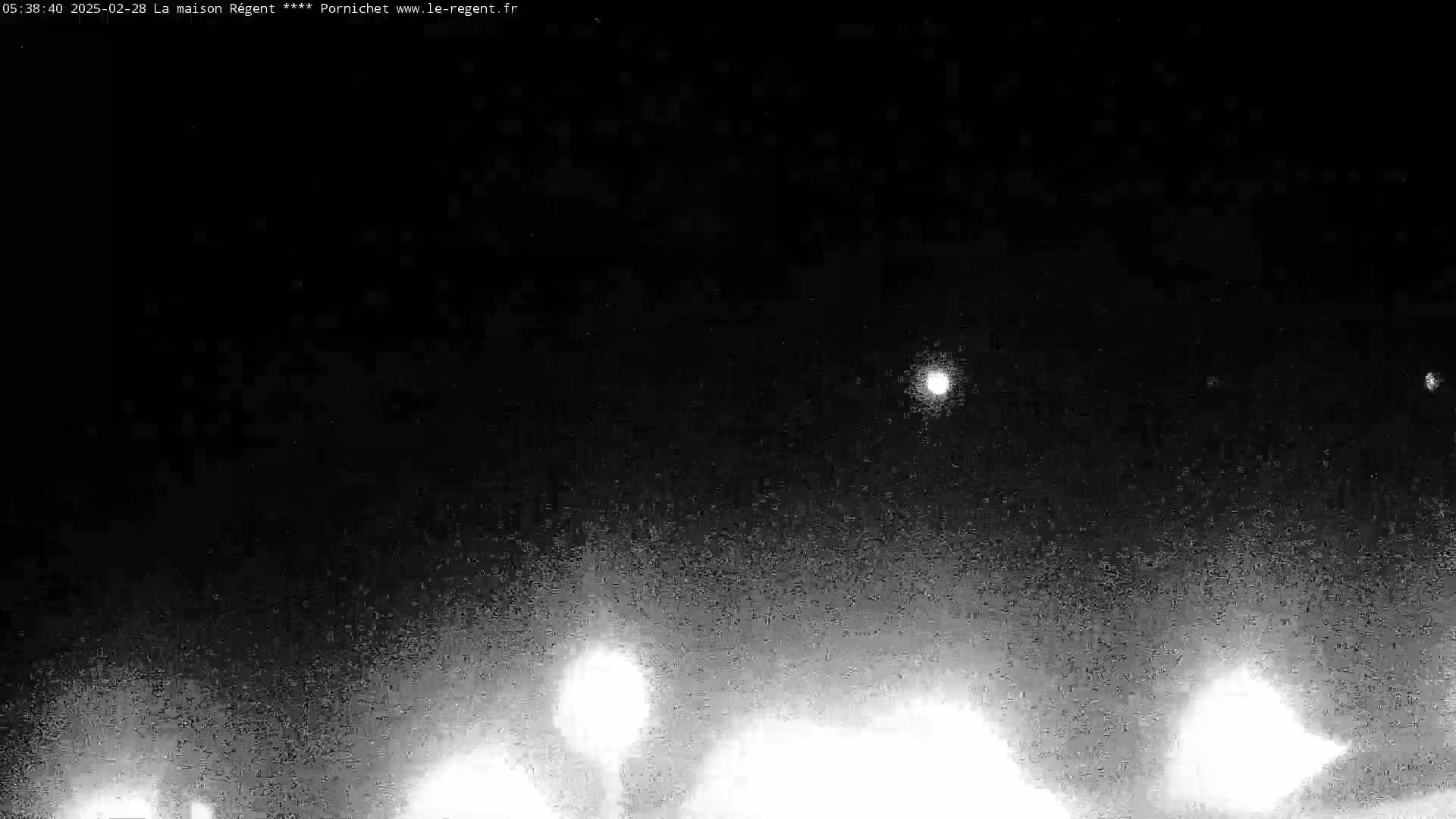 A nighttime, low-light outdoor image shows a dark sky with a few bright lights visible in the distance and some brighter lights closer to the bottom.