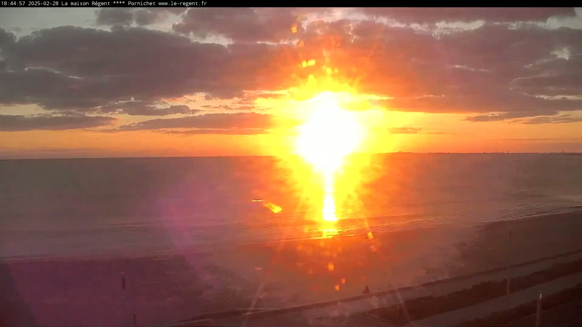 A bright, fiery sunset over a calm ocean beach.
