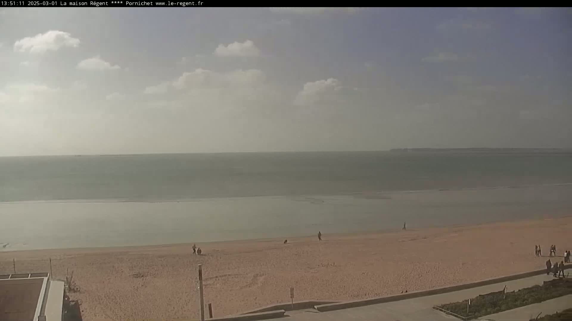 A sandy beach stretches out to a calm ocean under a partly cloudy sky.