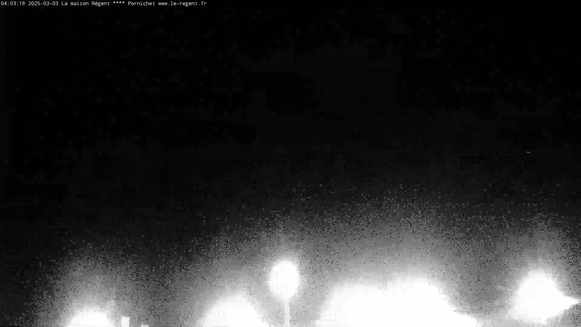 A nighttime, grainy image shows bright lights in the distance against a dark sky.