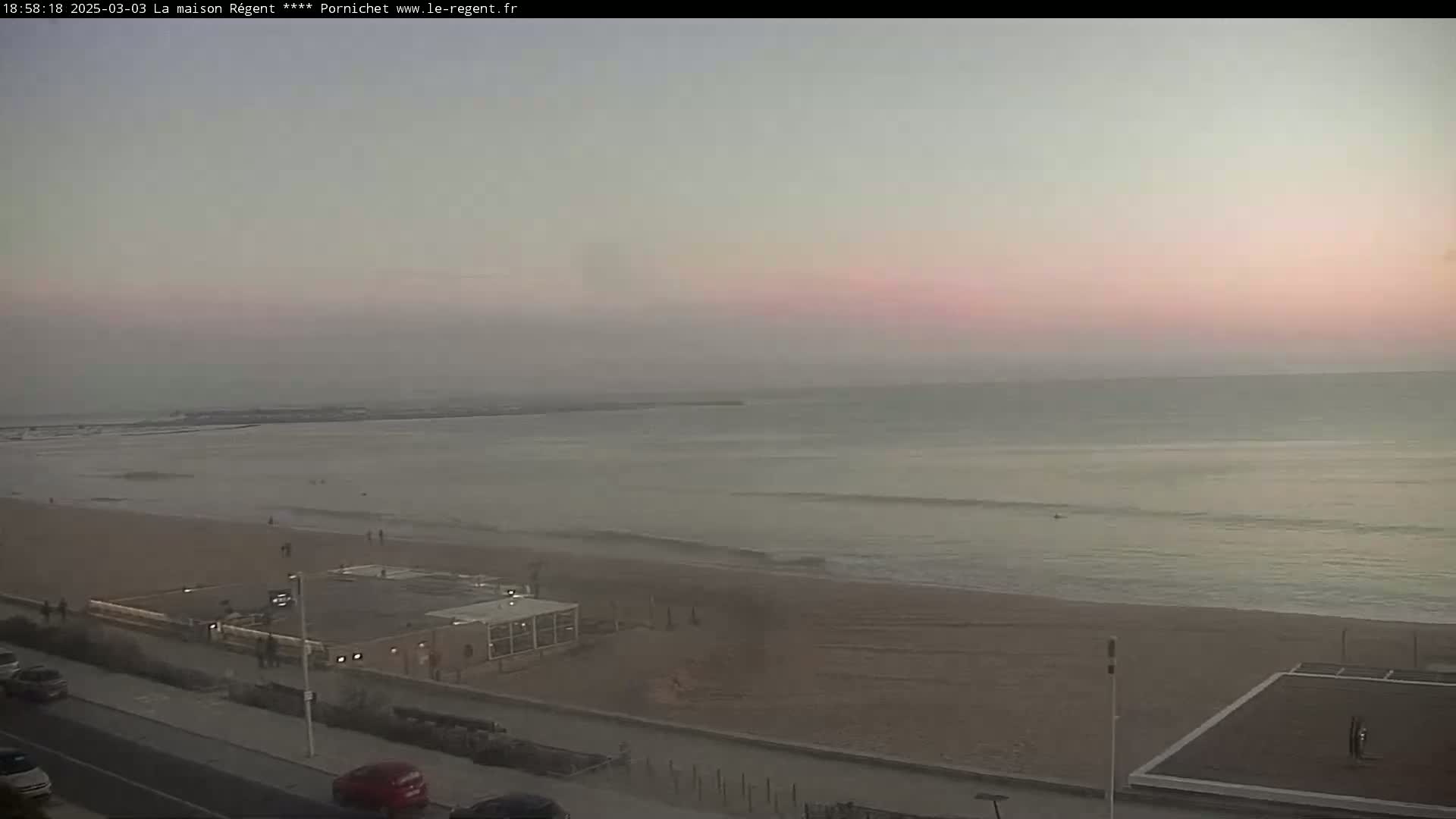 A beach with a calm ocean under a pale pink sunset.