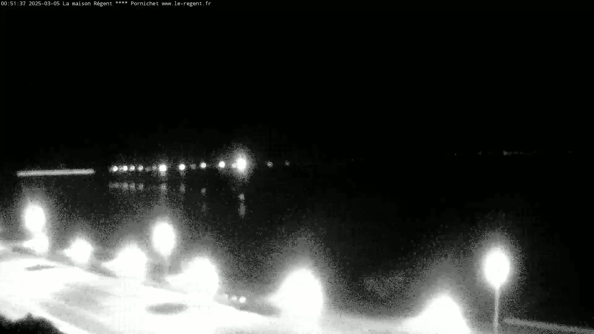 A nighttime view of a dark body of water reflecting lights from a roadway and street lamps along a shoreline.