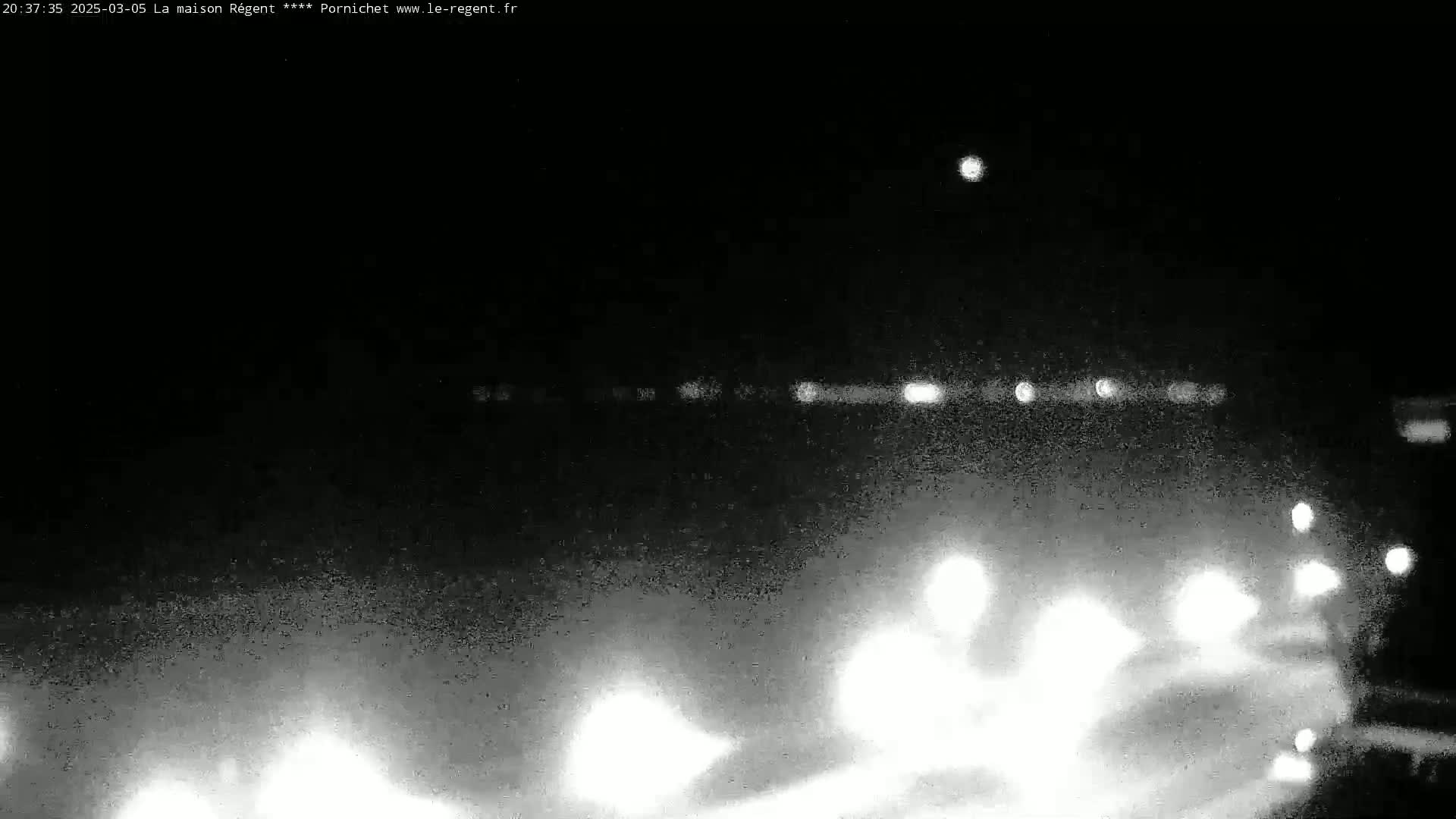 A nighttime, grainy image shows blurred lights of vehicles on a road, with a single bright light in the sky.