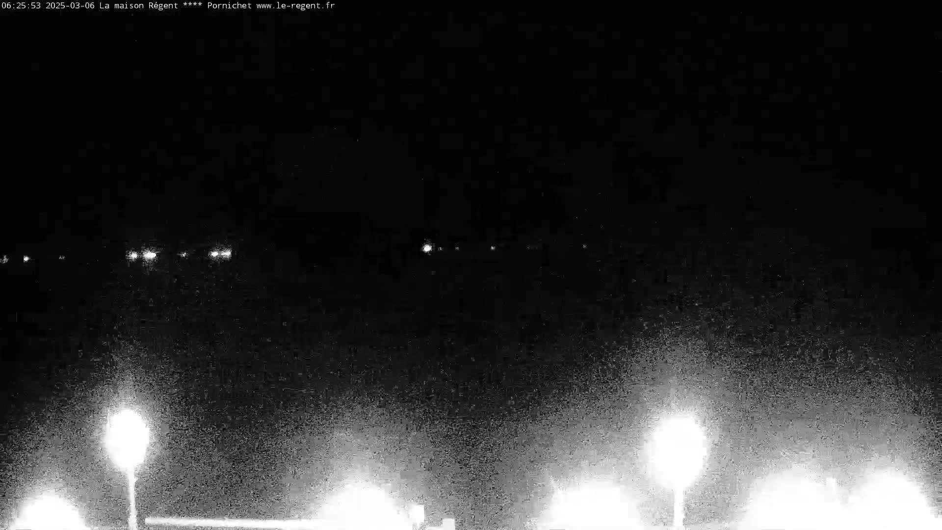 At night, under a dark sky, several distant lights are visible, along with brighter lights closer to the foreground that appear to be streetlights.