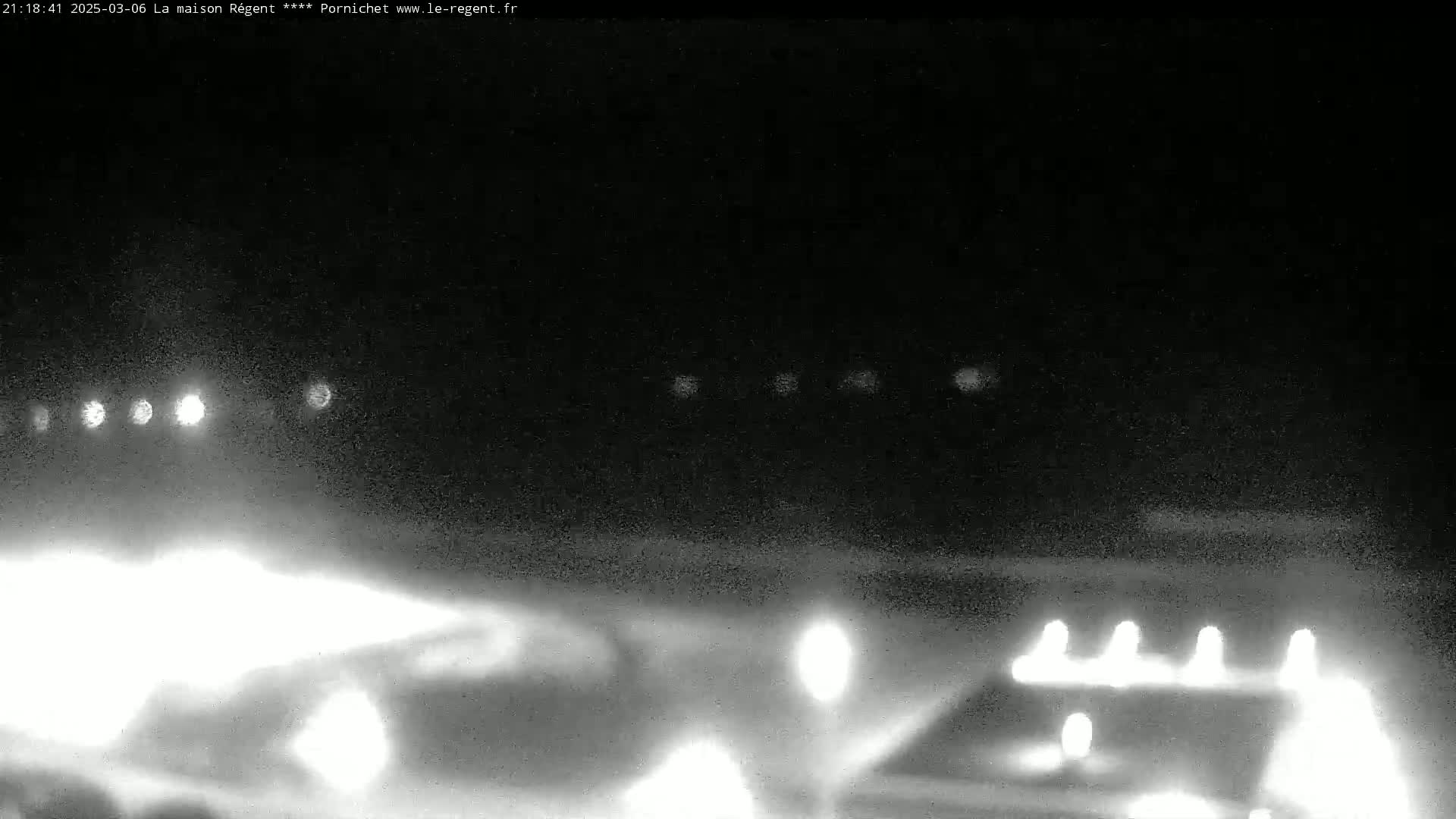 A nighttime, low-light image shows bright lights in the distance and a few closer lights near the bottom of the frame, possibly illuminating a building or parking lot.