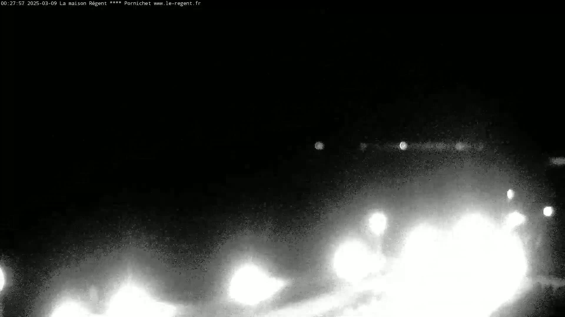 A nighttime, low-visibility outdoor scene shows bright headlights of vehicles approaching from a distance on a road.