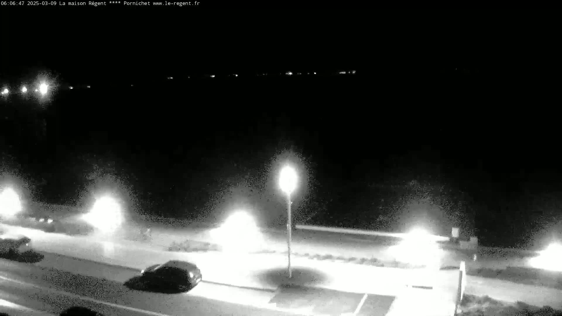 A nighttime, low-light view of a road with cars and streetlights, beside a dark body of water.