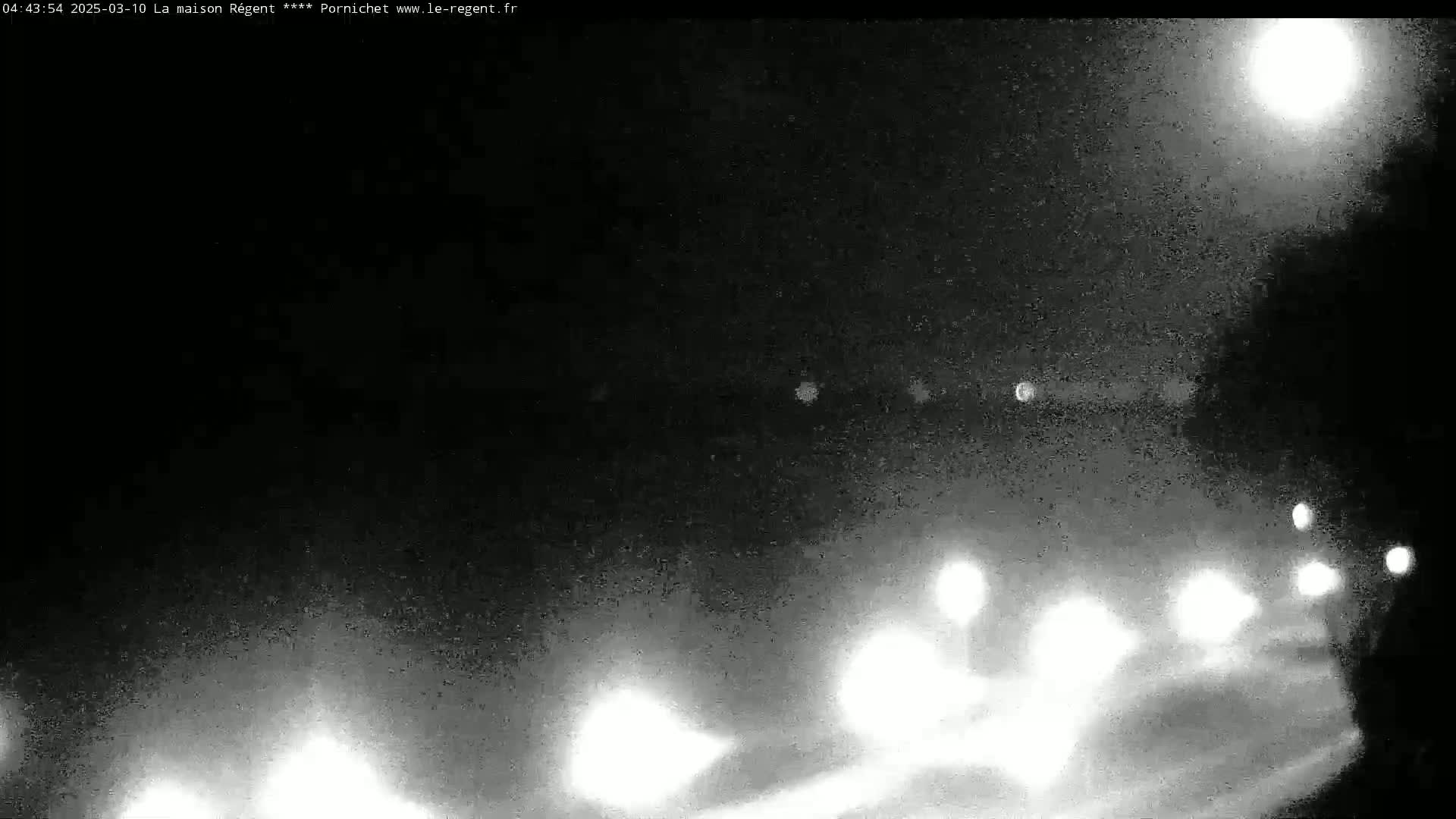 A nighttime, low-light view shows blurry headlights of vehicles traveling on a road under a bright moon.