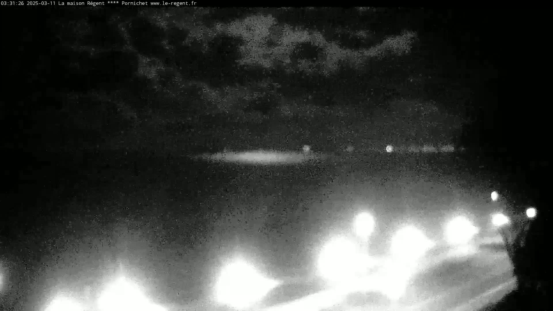 A nighttime, cloudy view of a road with headlights from approaching vehicles visible in the foreground.