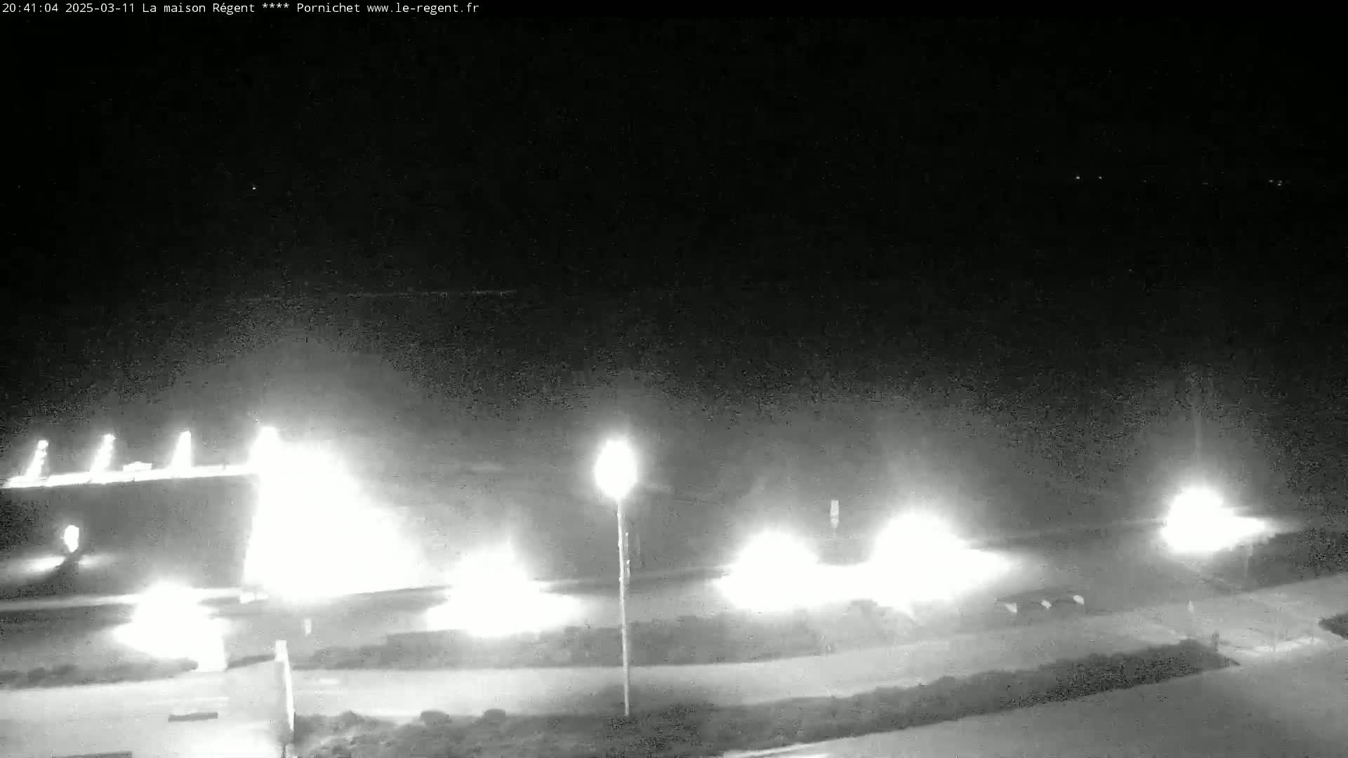 A nighttime, hazy scene shows bright lights illuminating a roadway and surrounding areas.
