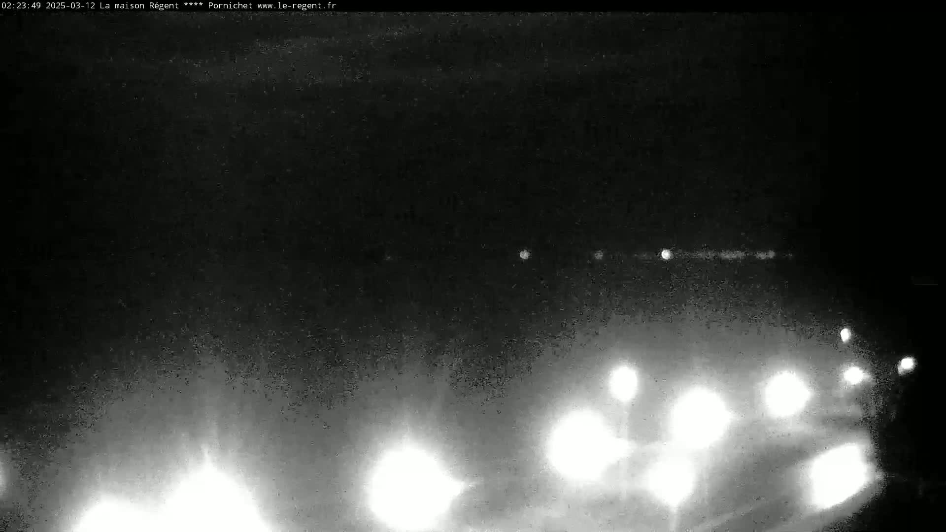 At night, bright headlights from several vehicles are visible on a dark road, with a hazy or foggy atmosphere.
