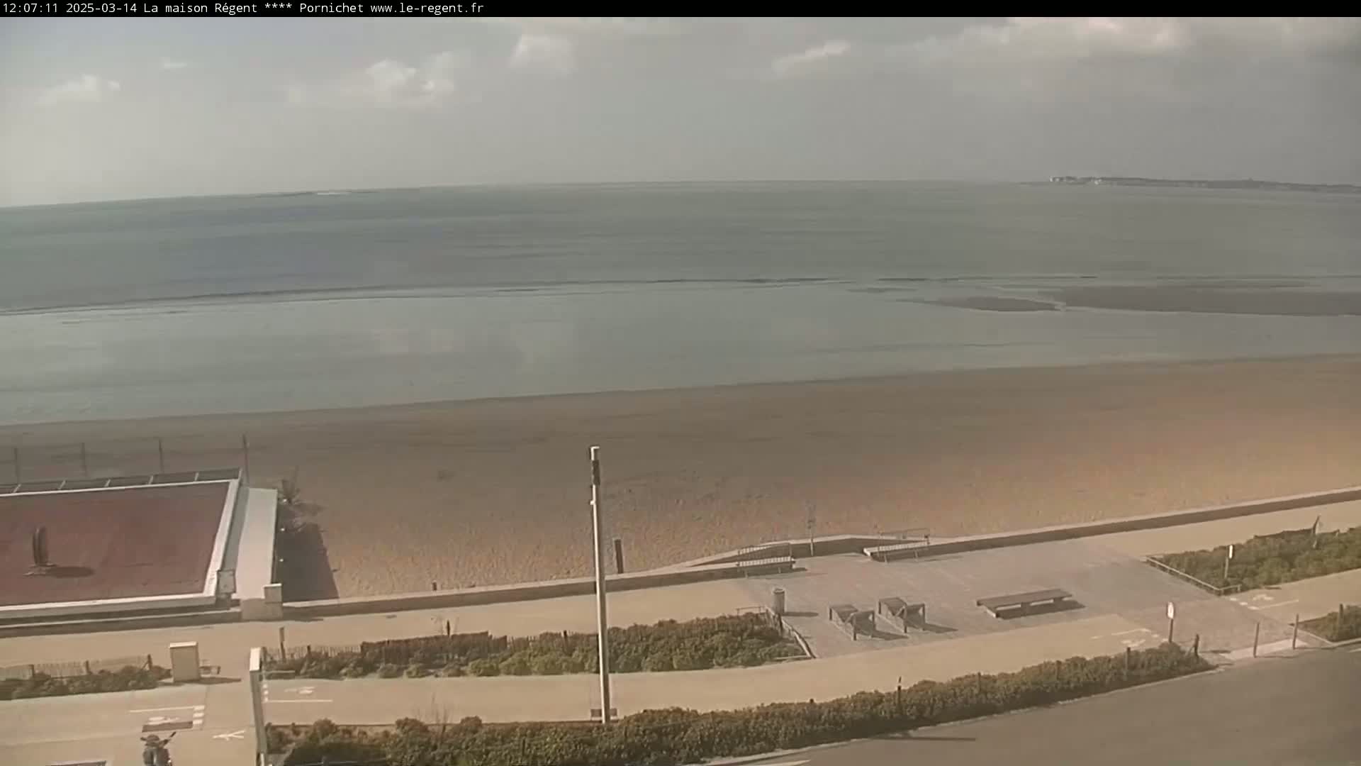 An expansive sandy beach stretches towards a calm ocean under a partly cloudy sky.