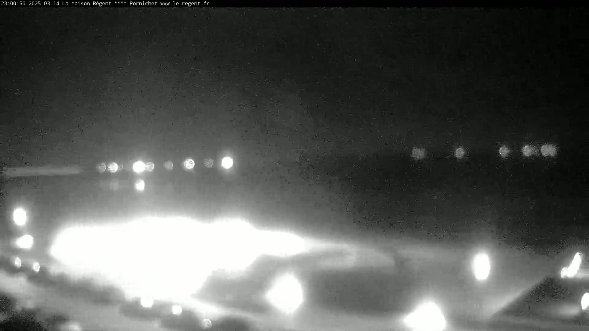A nighttime, low-light view of a road with blurry headlights of oncoming vehicles in the distance.
