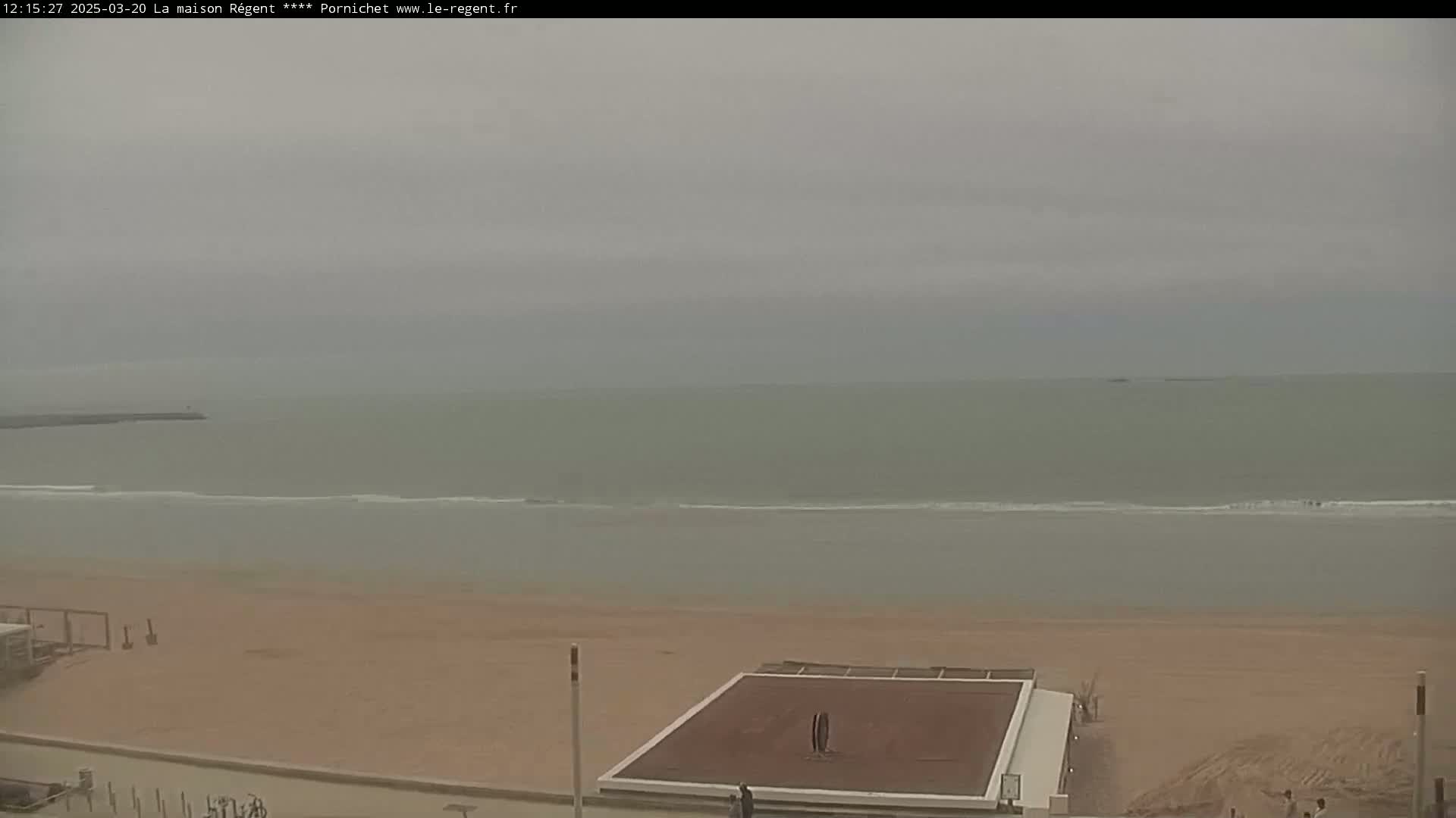 A sandy beach stretches to a calm, gray ocean under an overcast sky.