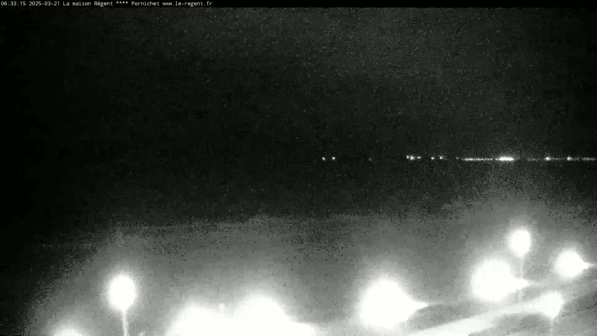 A nighttime, low-light view shows a dark landscape with a distant line of lights and several closer bright lights possibly from street lamps.