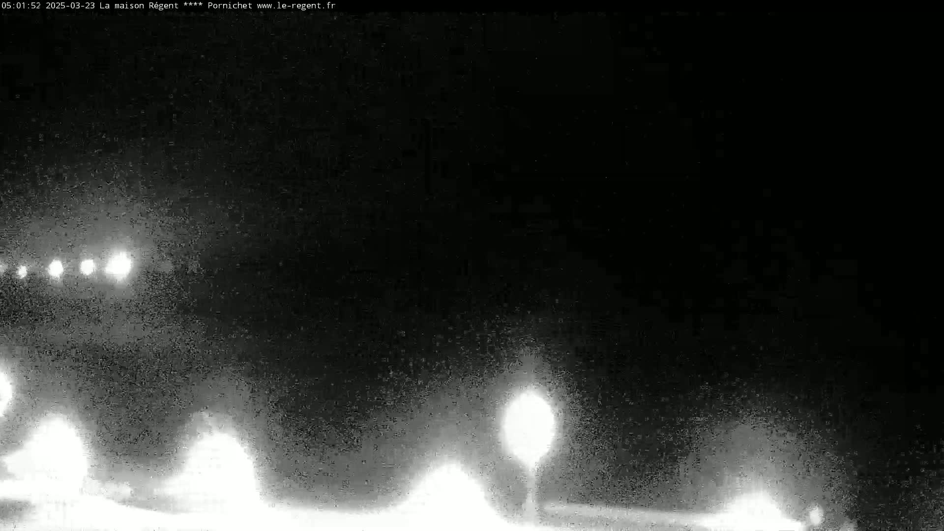 At night, in hazy or foggy conditions, headlights from several vehicles are visible on a road with indistinct streetlights.