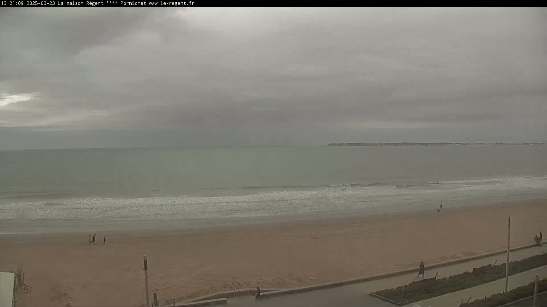 A sandy beach with gentle waves under an overcast sky.