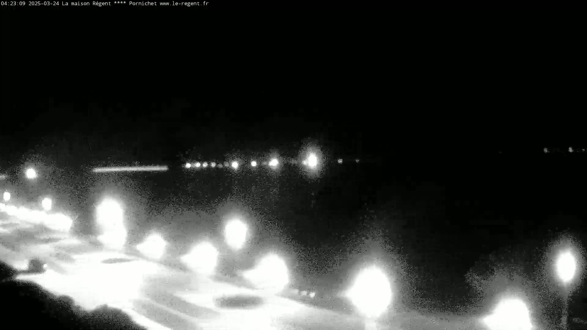 A nighttime, low-light view of a road with several vehicles traveling in both directions, illuminated by headlights and streetlights.
