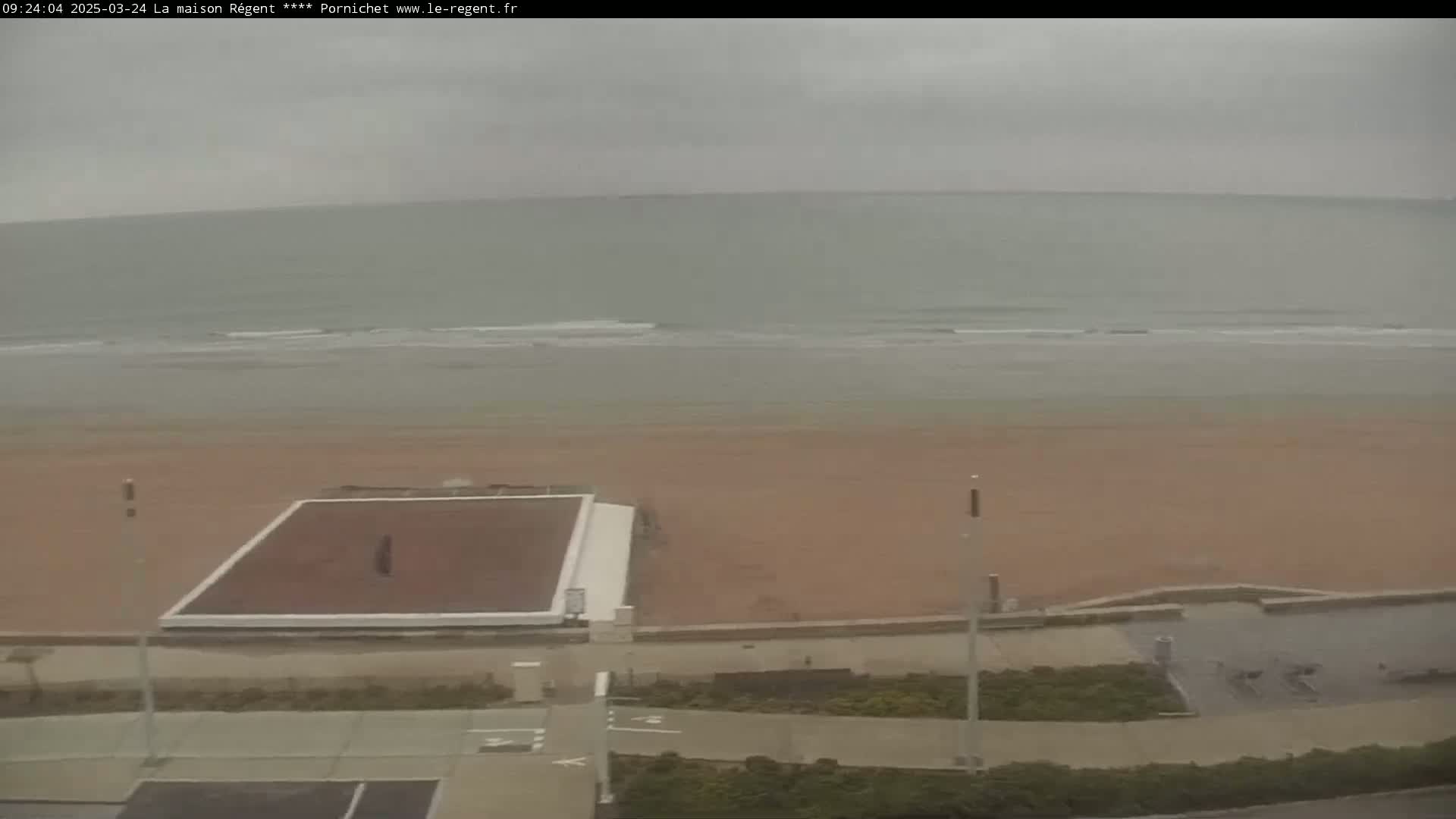 A mostly empty beach with a flat, dark-colored court visible near a walkway is seen on an overcast day.