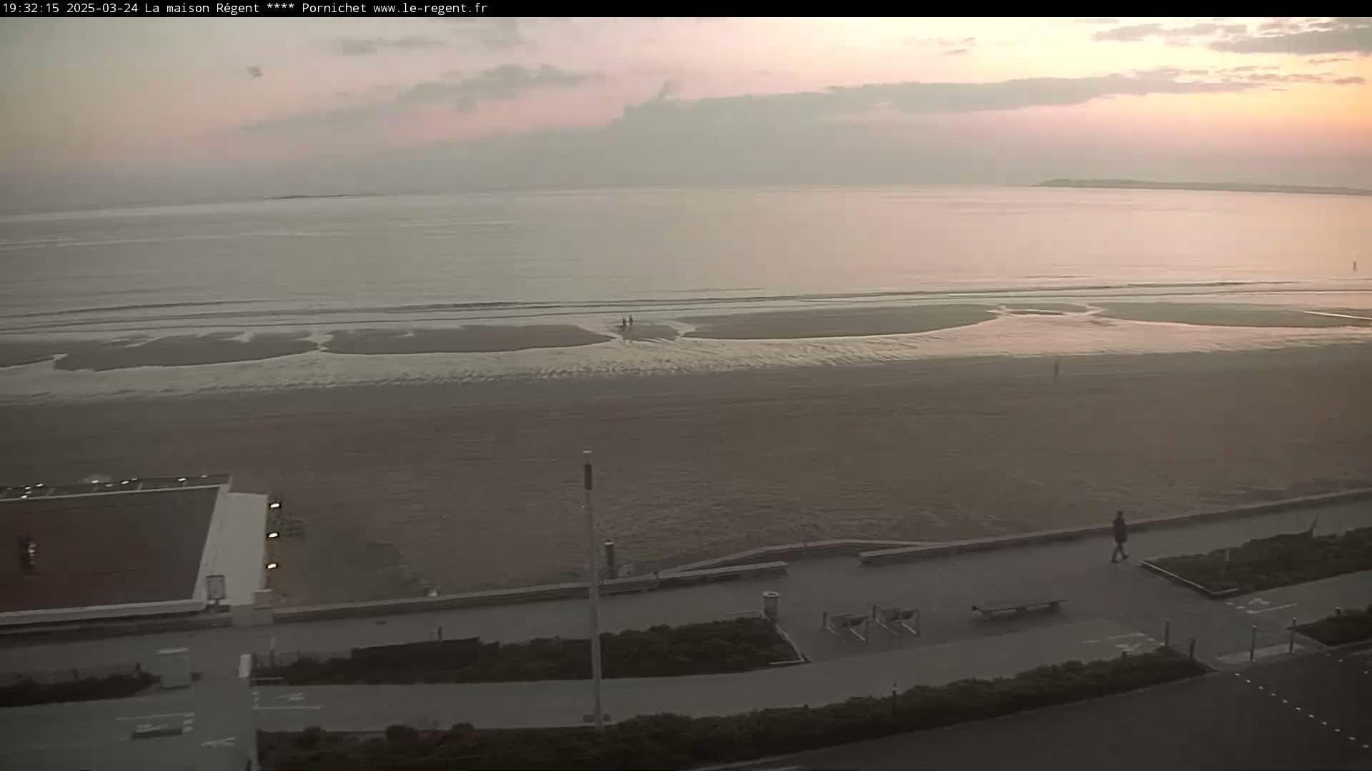A wide, sandy beach stretches to a calm sea under a dusky, pinkish sky.