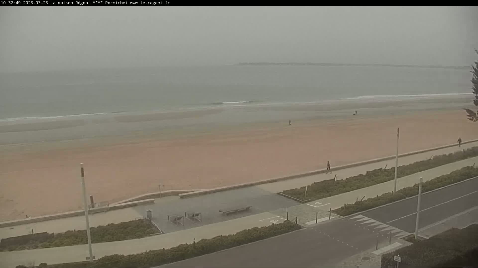 A wide, sandy beach stretches to a calm, gray sea under an overcast sky.