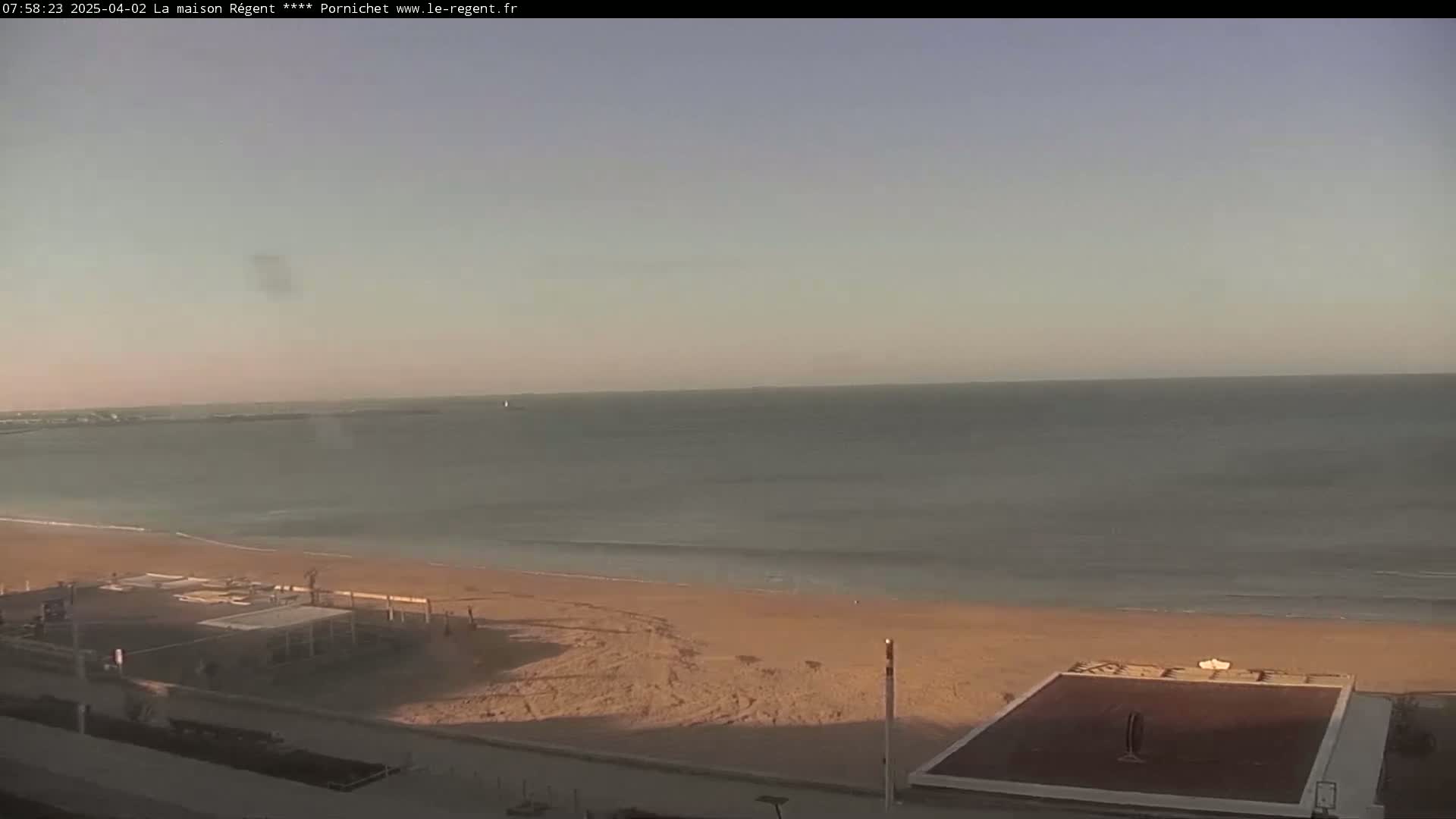 A sandy beach stretches along a calm ocean under a clear, pale sky.