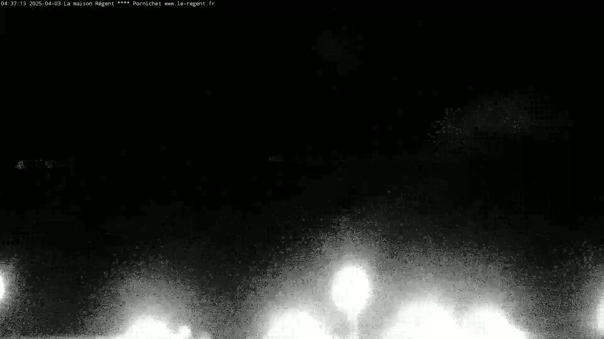 A nighttime, low-light outdoor scene shows blurry, bright lights at the bottom, possibly from vehicles' headlights, against a mostly dark background.