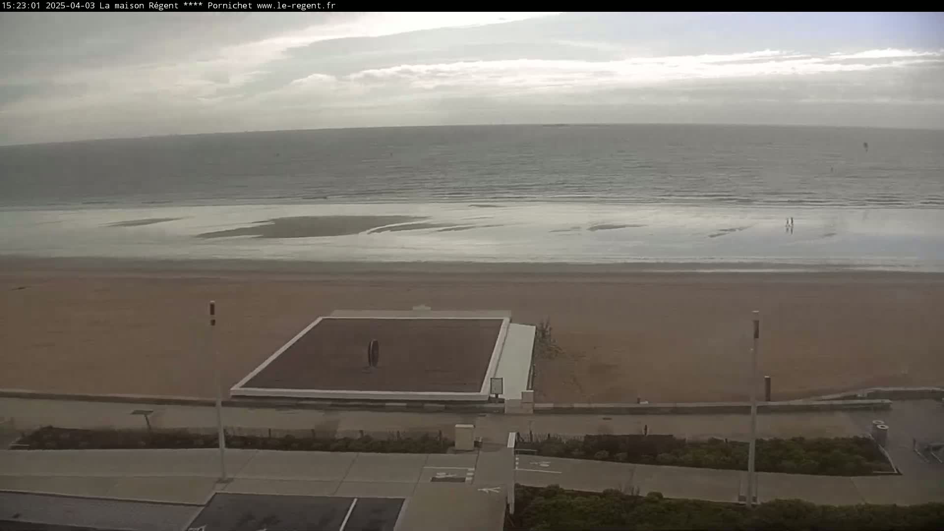 A beach with a volleyball court is seen from an elevated vantage point on an overcast day.