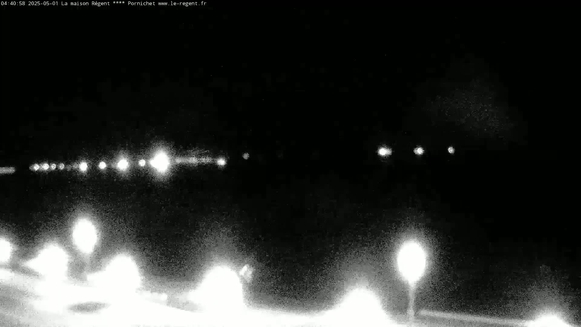 A nighttime, low-light image shows a road with vehicle headlights visible in the distance and nearby streetlights illuminating a snowy or icy ground.