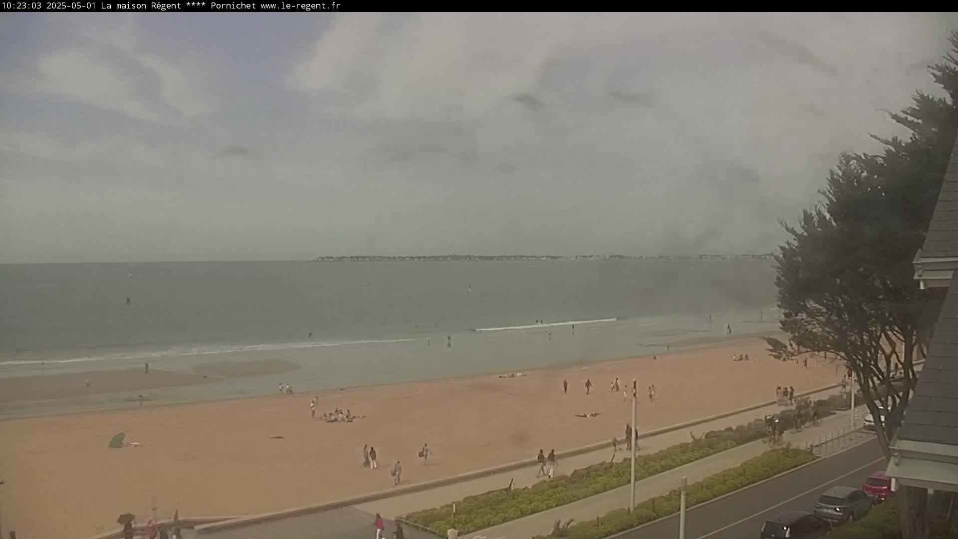 A mostly cloudy day reveals a sandy beach with scattered people, a calm ocean, and a distant shoreline.