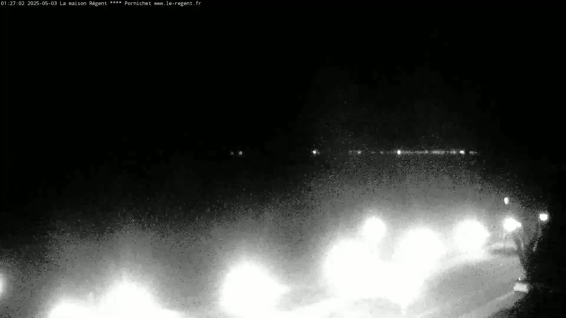 At night, bright headlights from vehicles are visible on a dark, possibly foggy or hazy road.