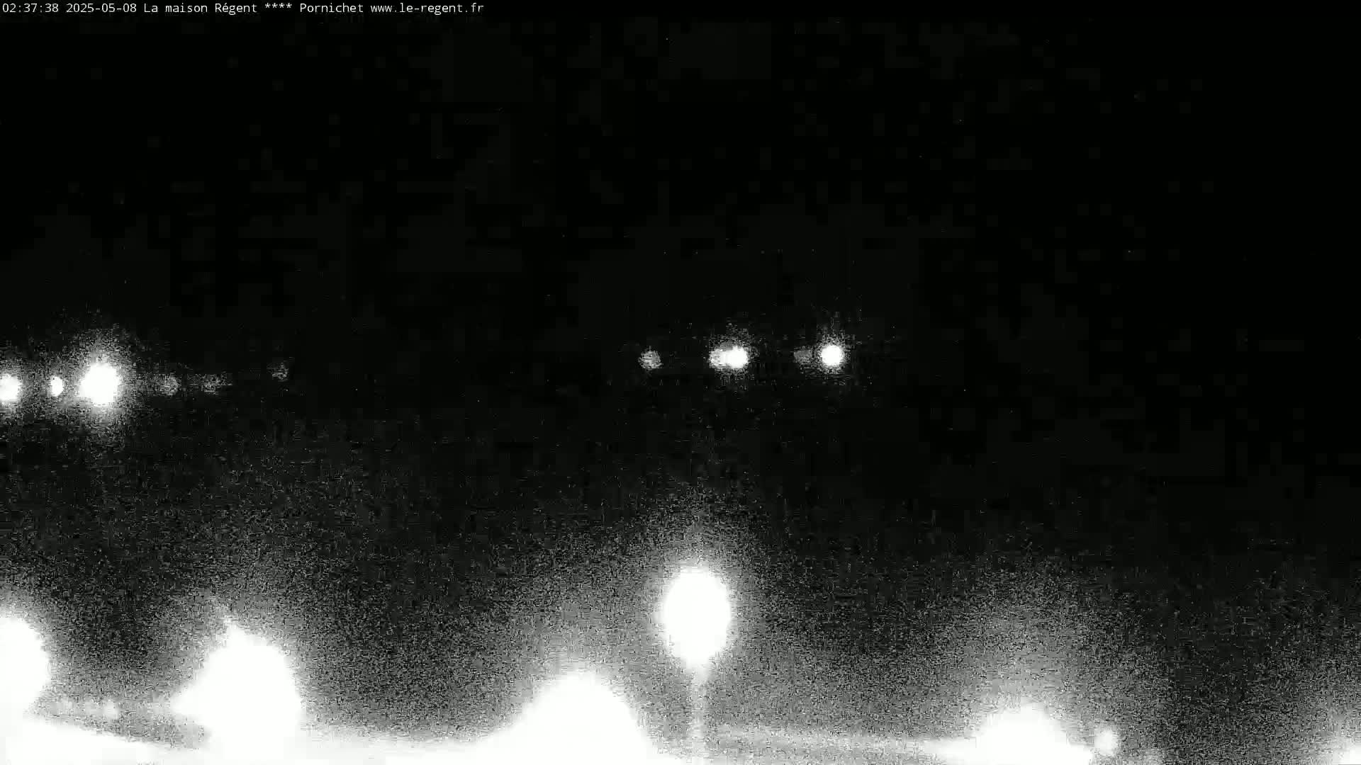 At night, the headlights of several vehicles are visible on a dark road, illuminated by a streetlight.