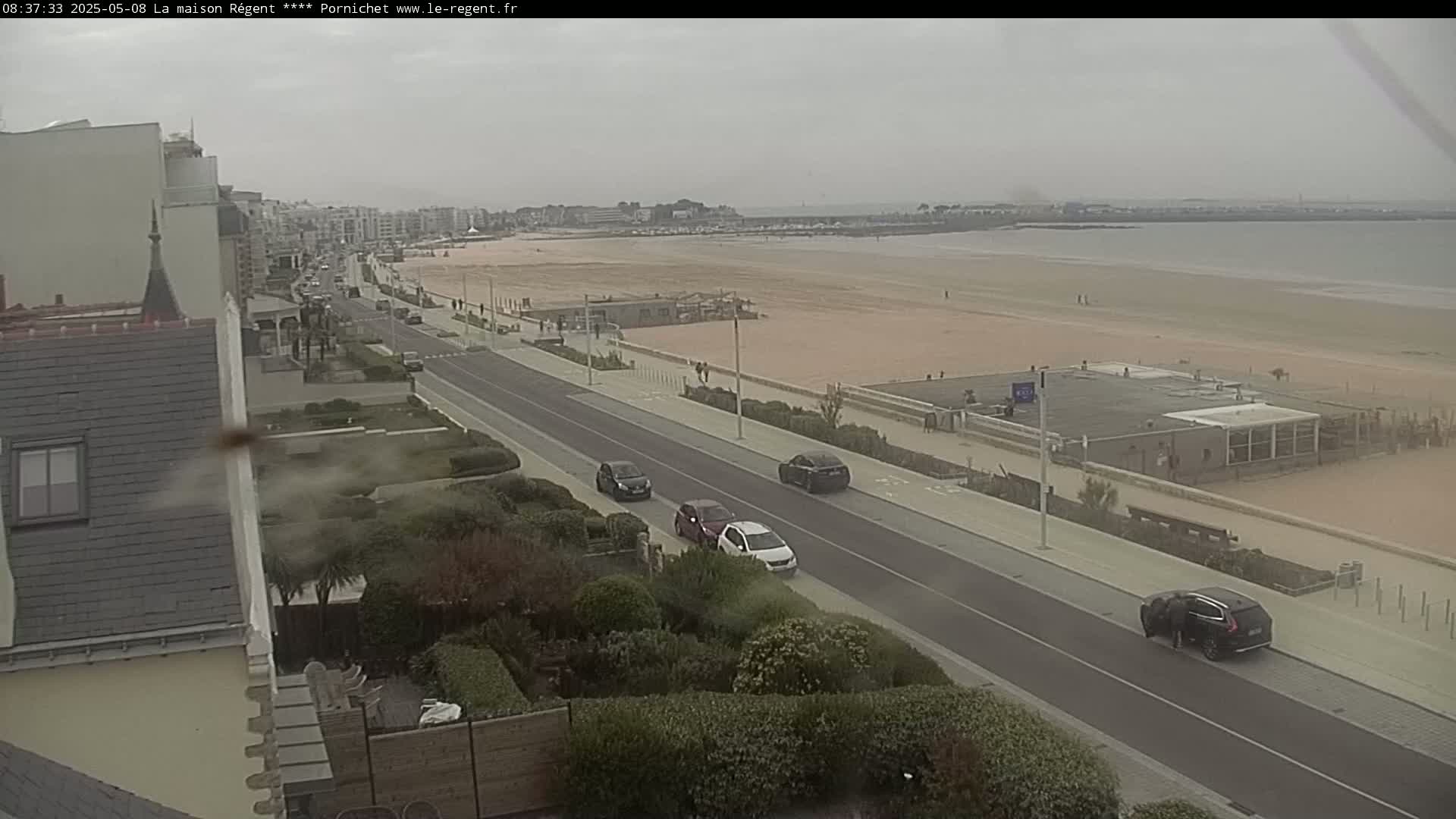 A coastal road with several cars and a sandy beach under an overcast sky.