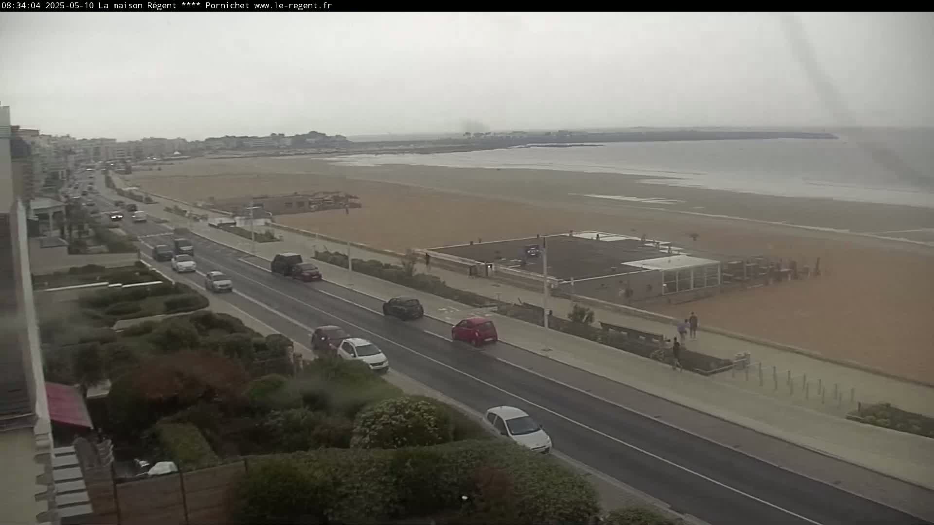 A beach with a few people and a road with several cars is visible under an overcast sky.