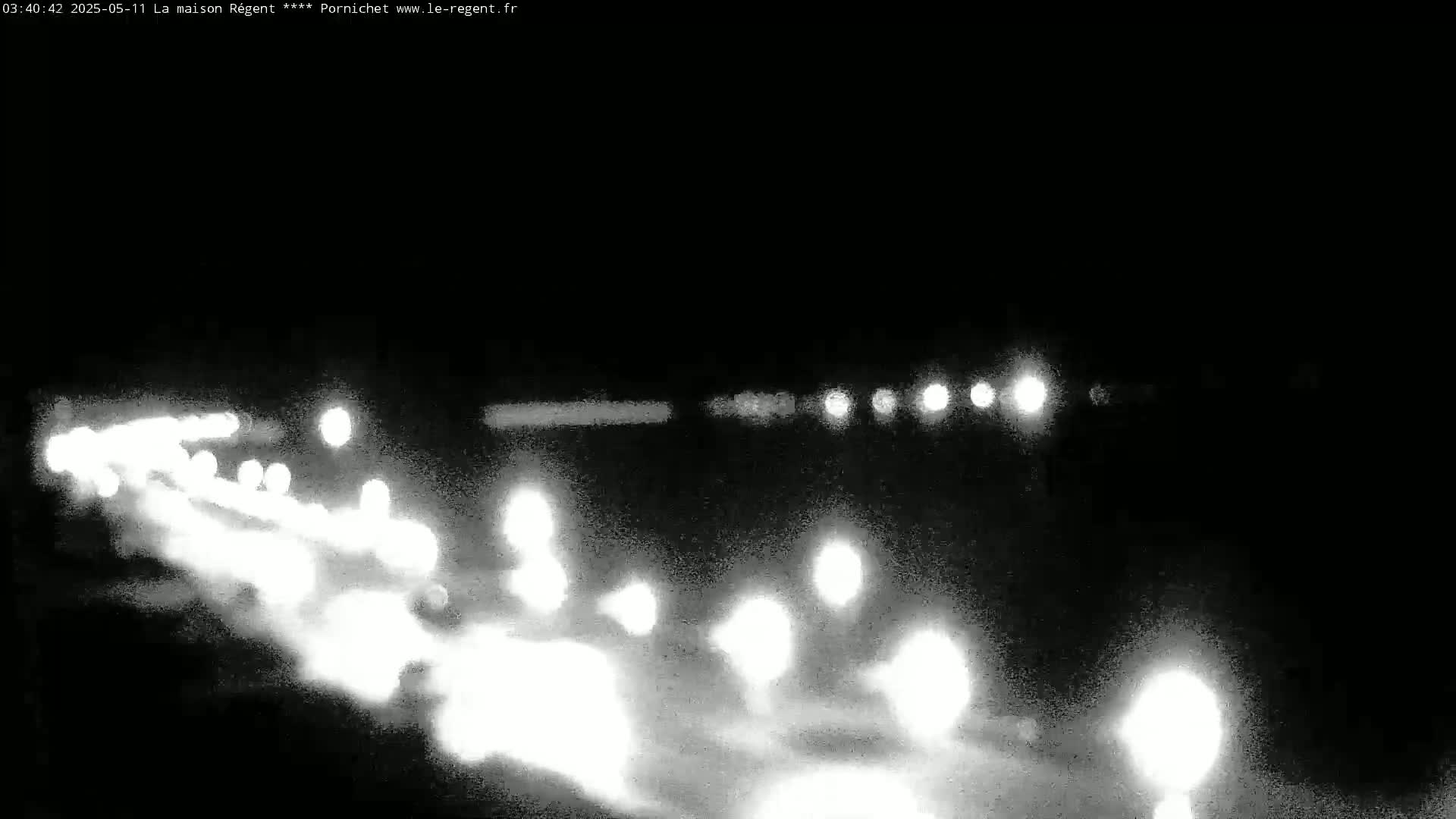 A nighttime, low-light image shows the blurry headlights of numerous vehicles traveling on a road.