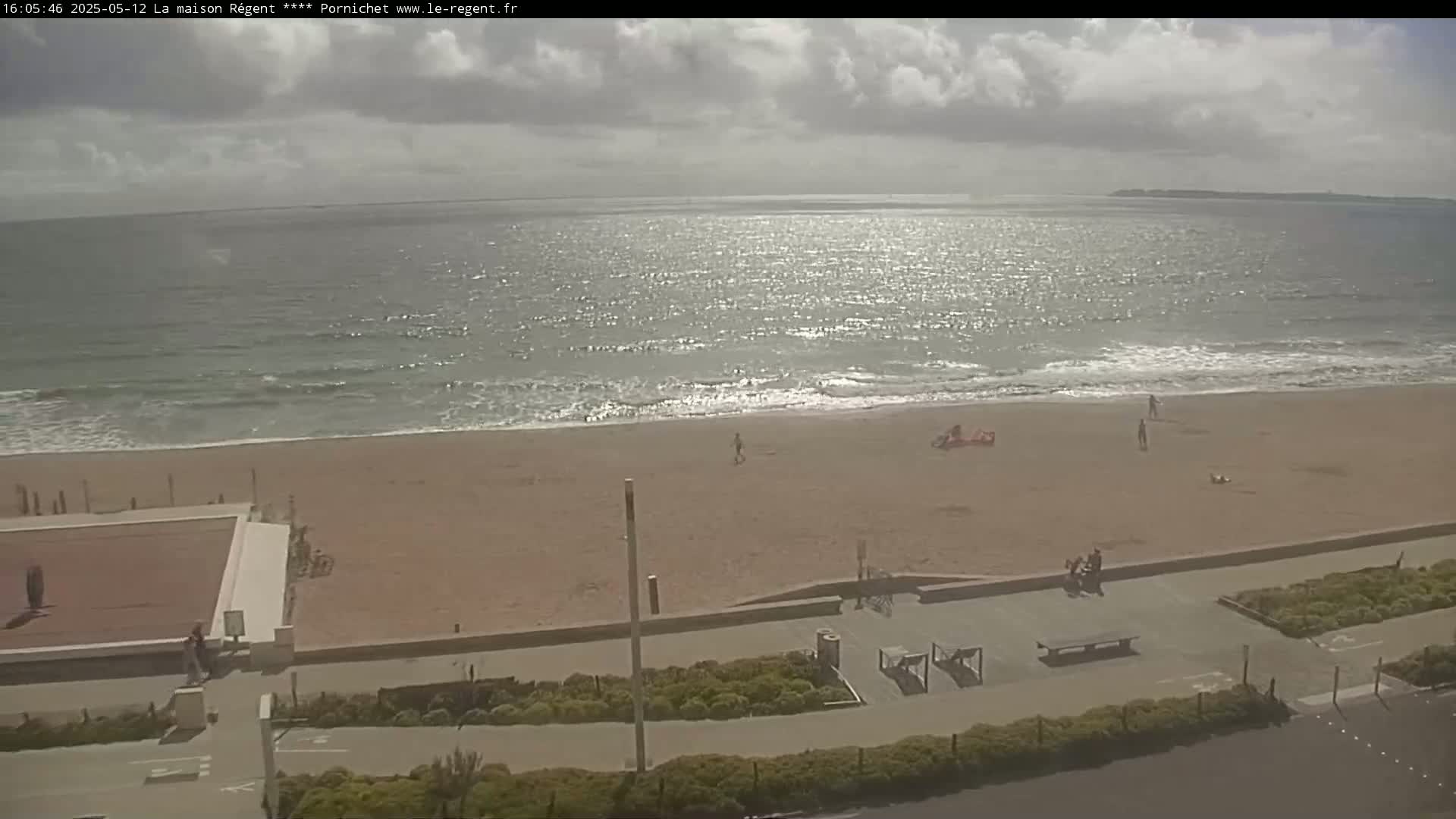 A partly cloudy day shows a beach with a few people on it and calm ocean waves.