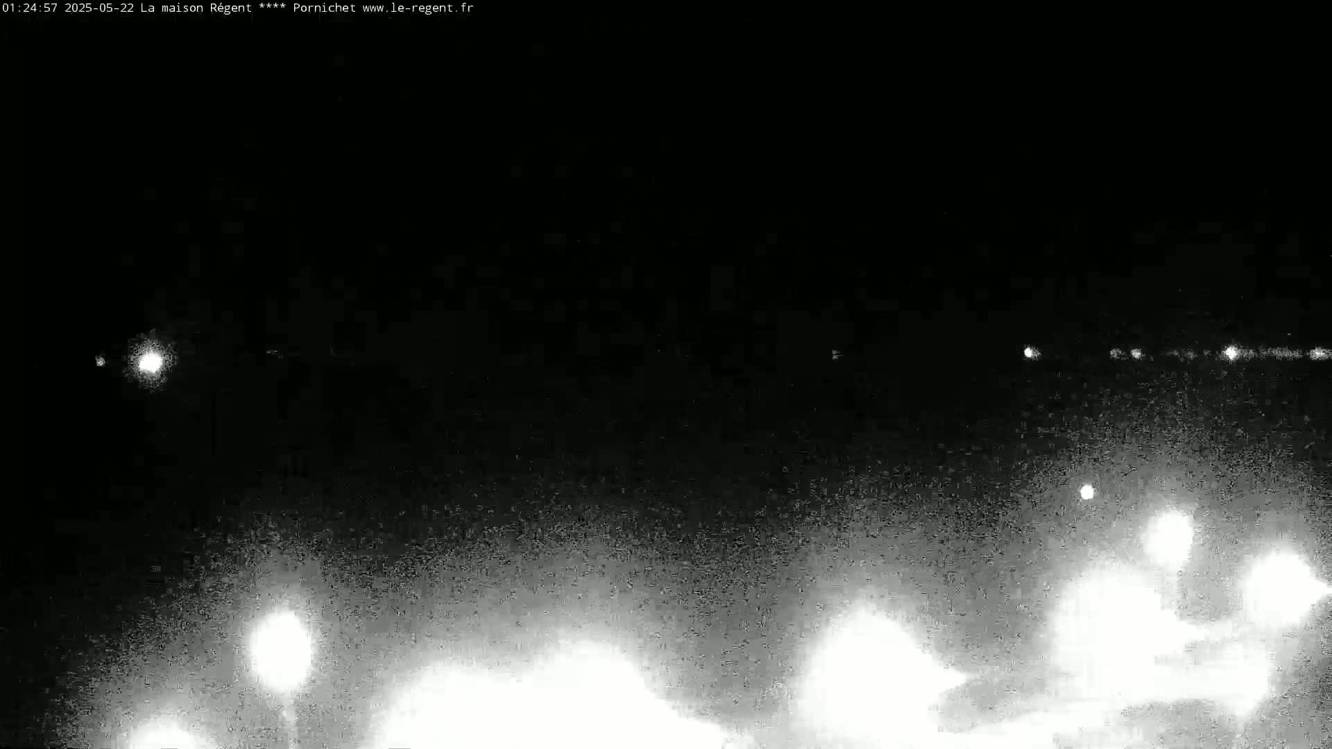A nighttime, low-light view shows blurry lights in the distance and some closer to the bottom, possibly streetlights, against a dark, grainy background.