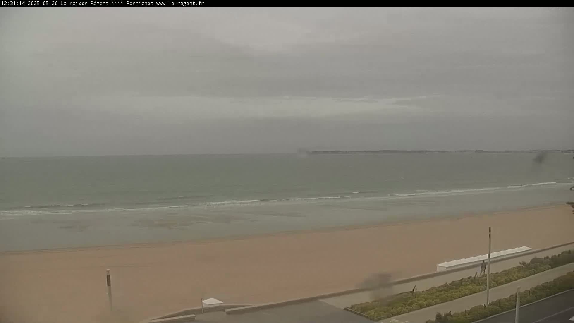 A wide sandy beach stretches to a calm, gray-toned ocean under an overcast sky.